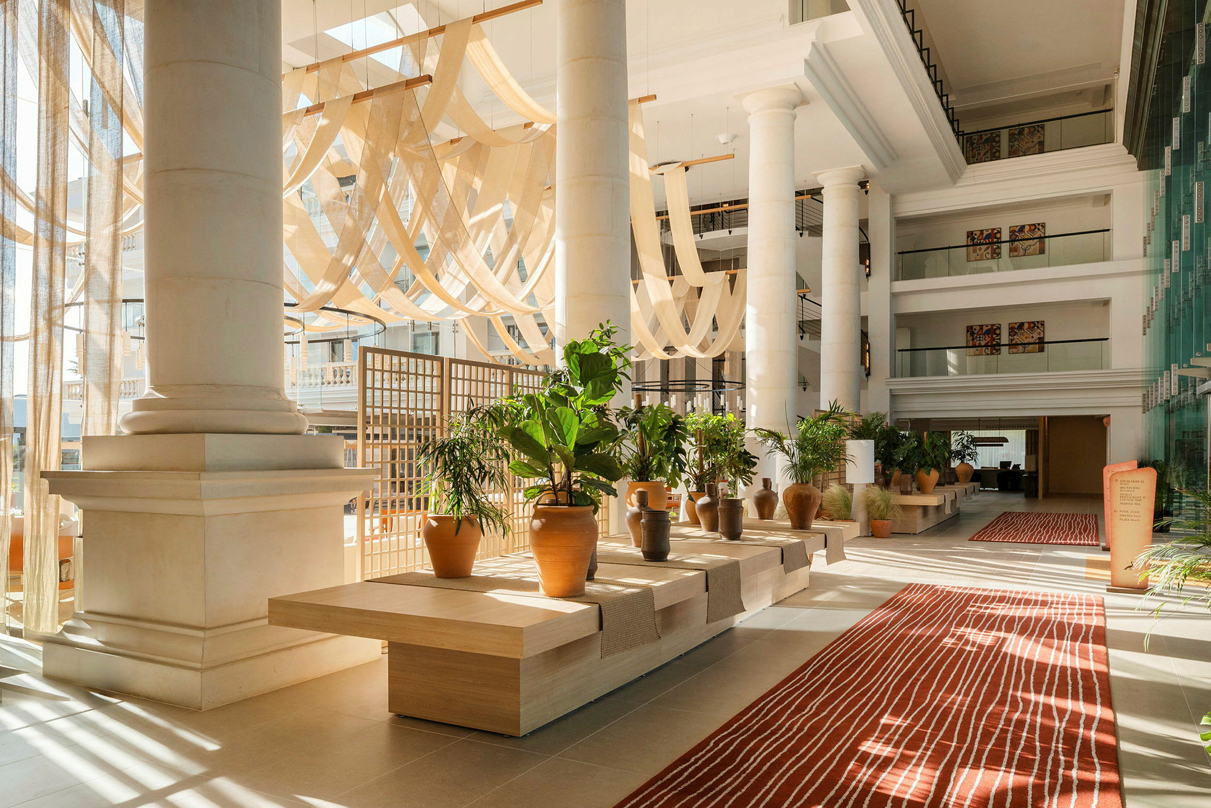 Lys og rummelig hotellobby med store søjler, dekorative planter og et rødt tæppe. (AI-genereret tekst)