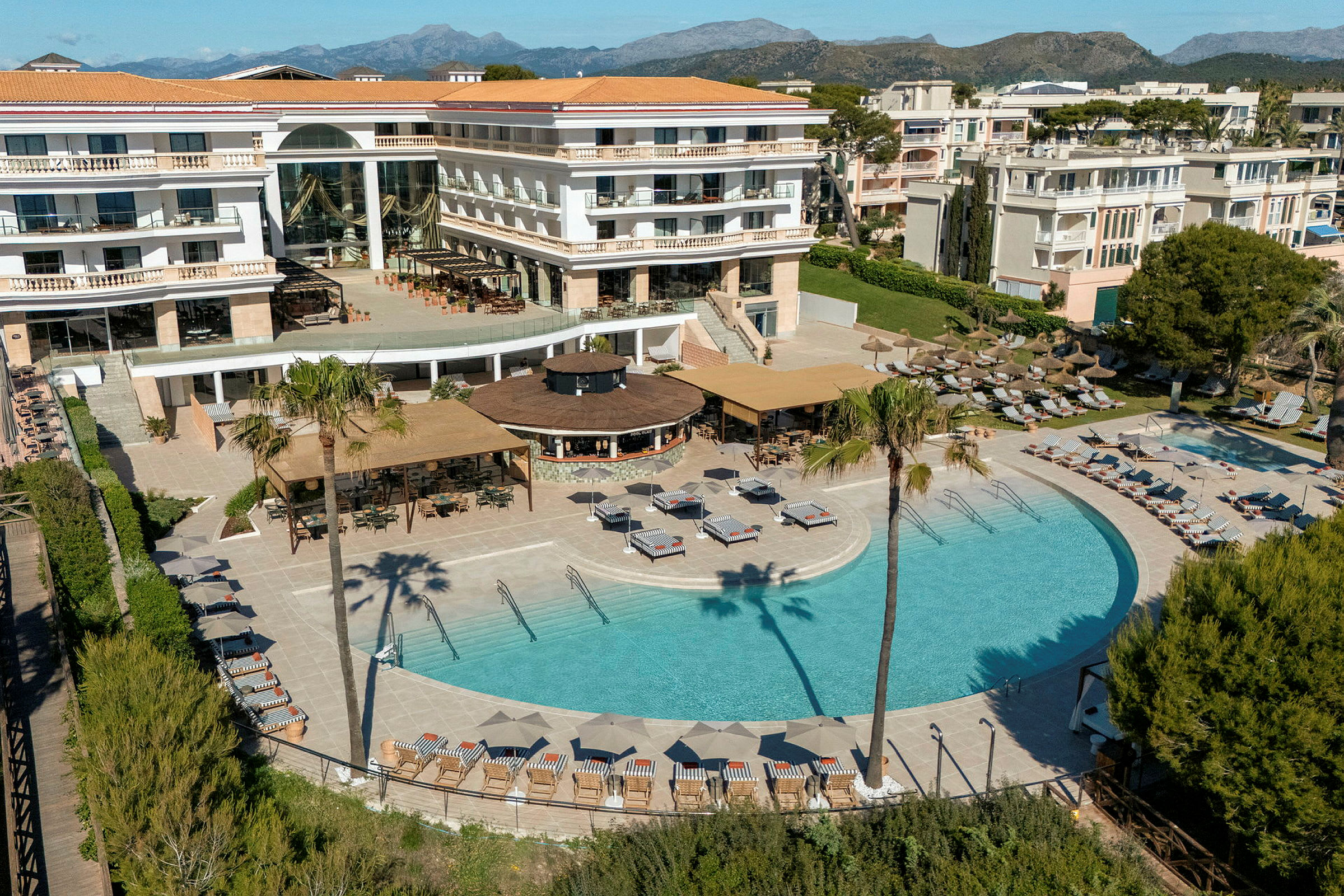 Hotel med pool- og terrasseområde omgivet af liggestole, parasoller og grønt. (AI-genereret tekst)