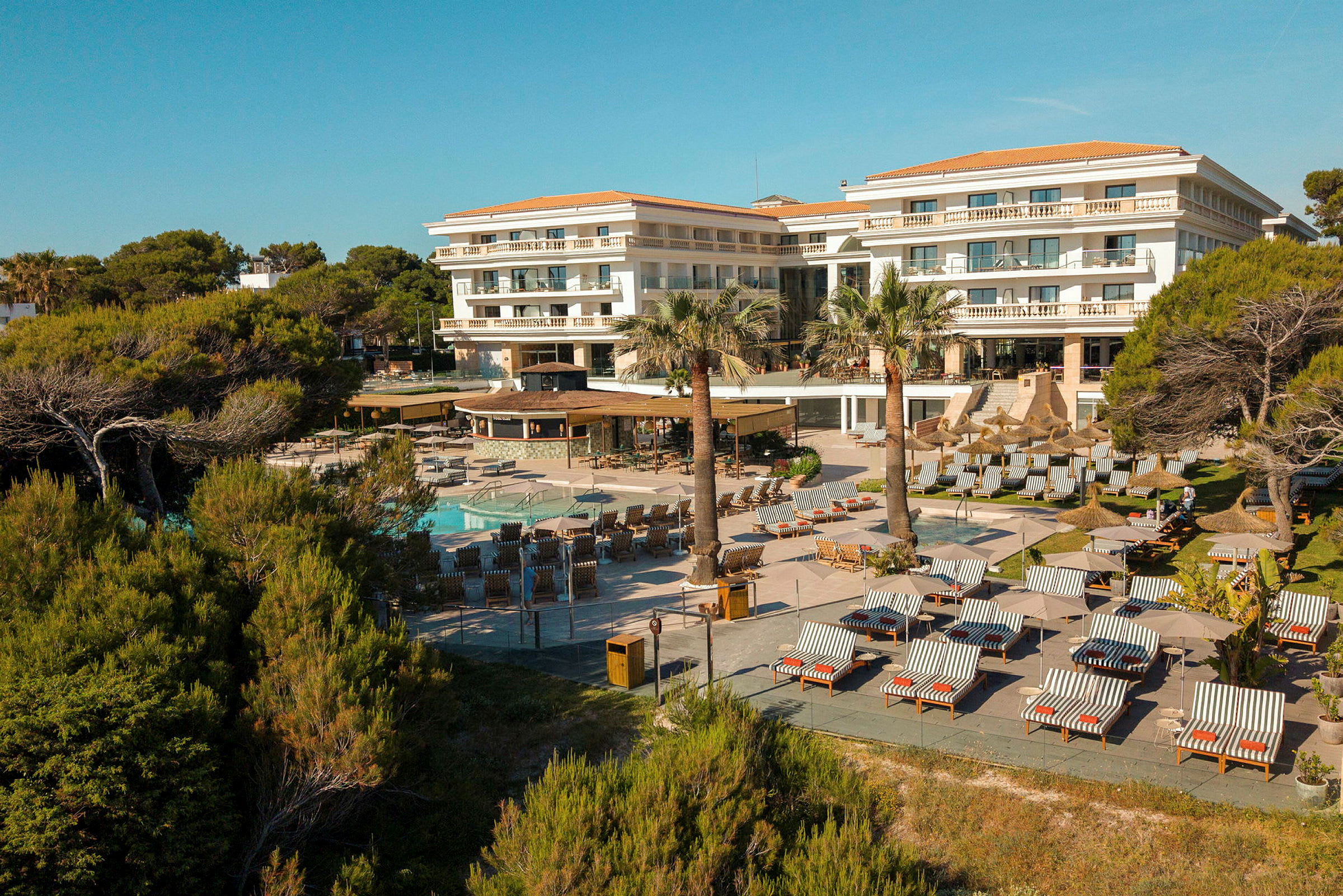 Et hotel med poolområde og solsenge omgivet af træer og grønne områder. (AI-genereret tekst)