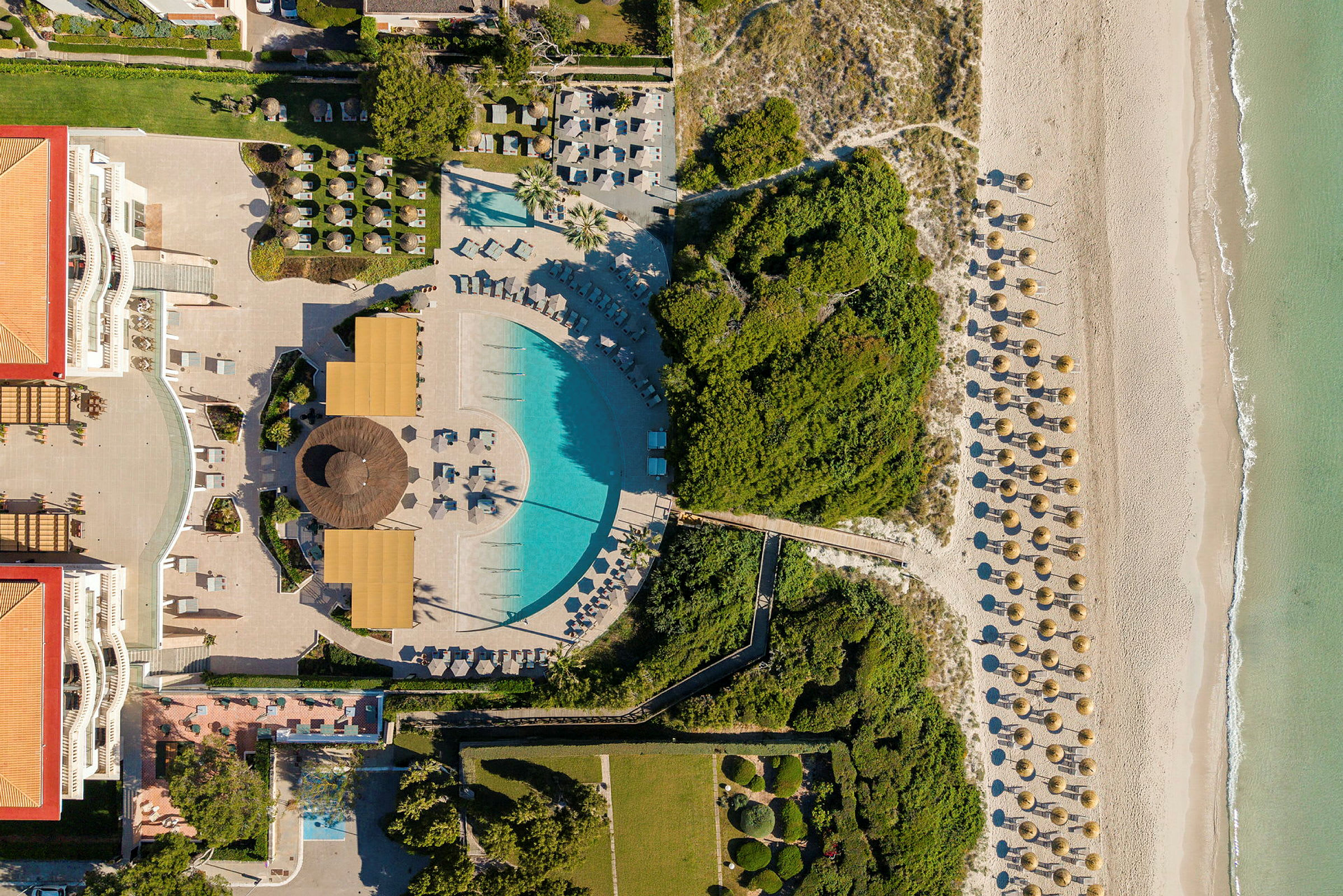 Luftfoto af et hotelområde med pool, grønne områder, en strand og parasoller. (AI-genereret tekst)