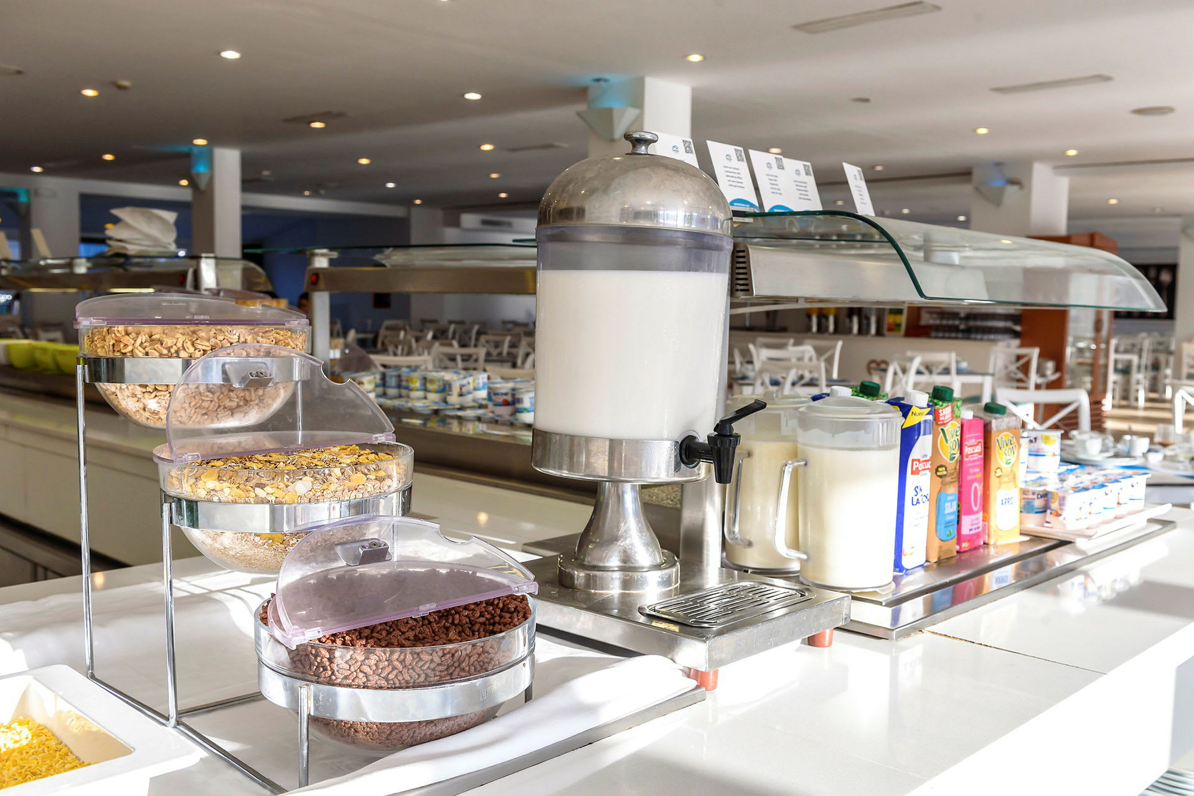 Billede af en hotelmorgenmadsbuffet med mælkedispenser, korn og juicekartoner. (AI-genereret tekst)
