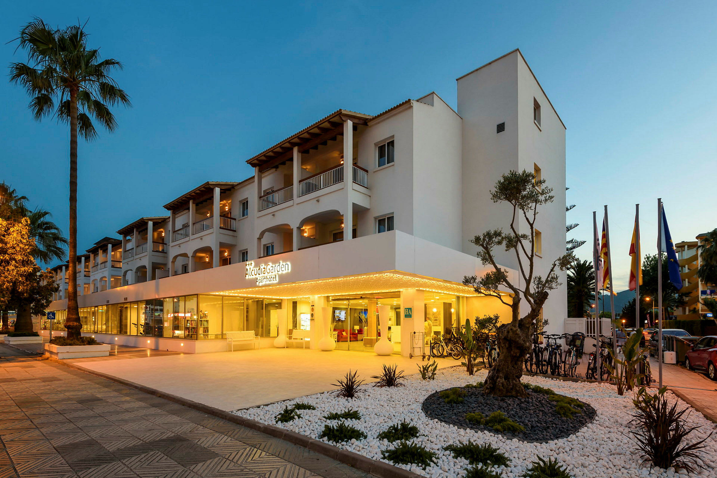 Billede af hotellet Alcudia Garden Aparthotel med oplyst indgang og omkringliggende have. (AI-genereret tekst)
