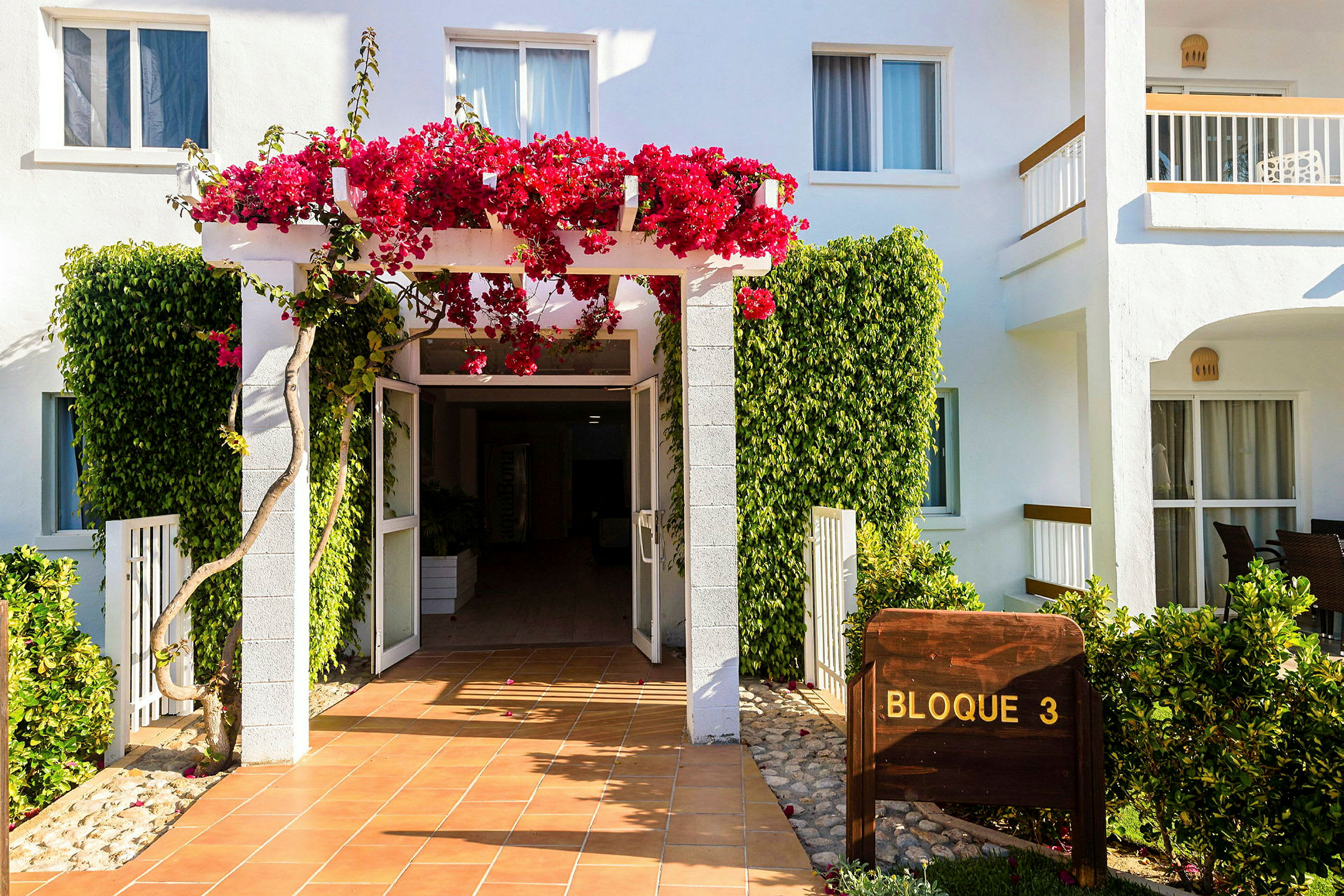 Indgangen til en bygning med hvide vægge og blomster klatrer på en pergola. (AI-genereret tekst)