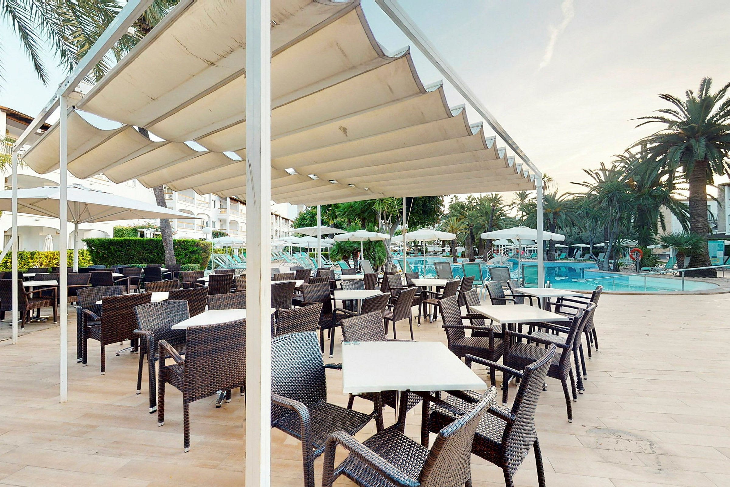 En udendørs terrasse med borde og stole under en pergola tæt ved en pool. (AI-genereret tekst)
