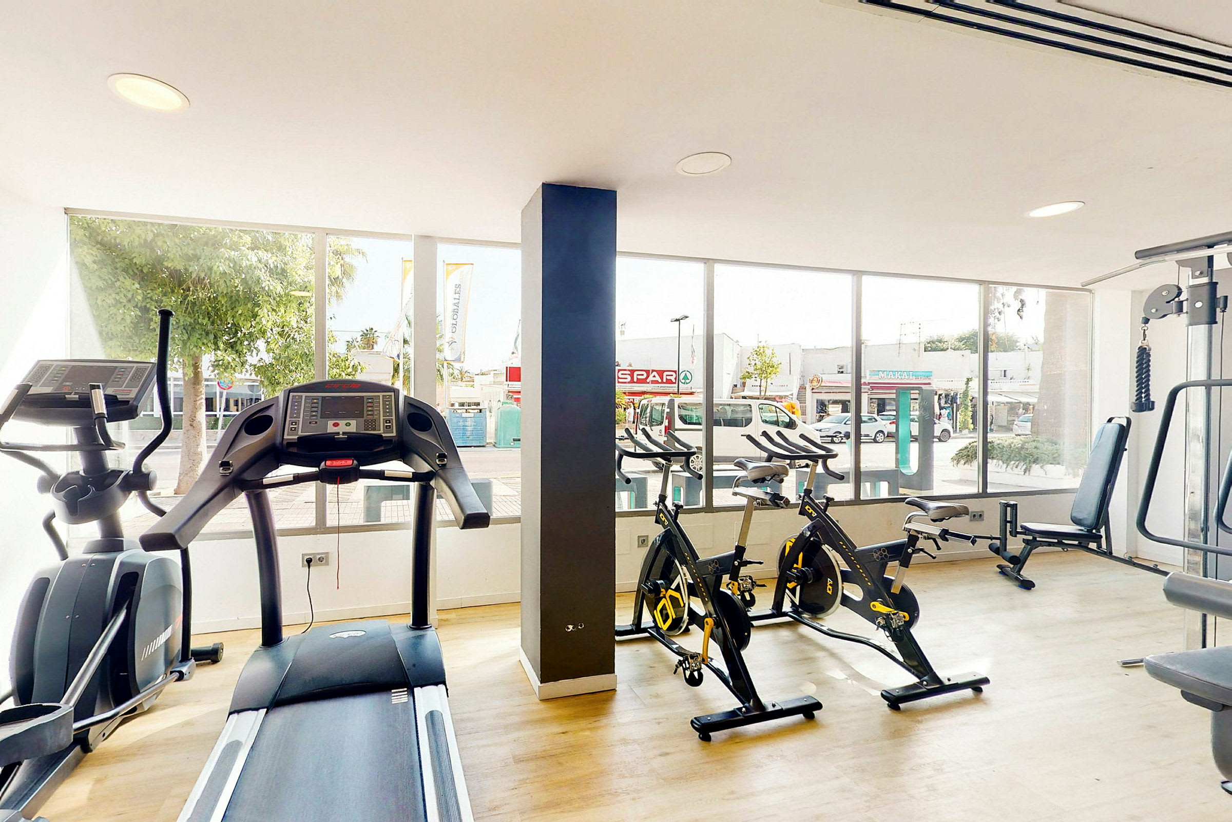 Et fitnessrum med træningsmaskiner, herunder løbebånd og motionscykler foran store vinduer. (AI-genereret tekst)