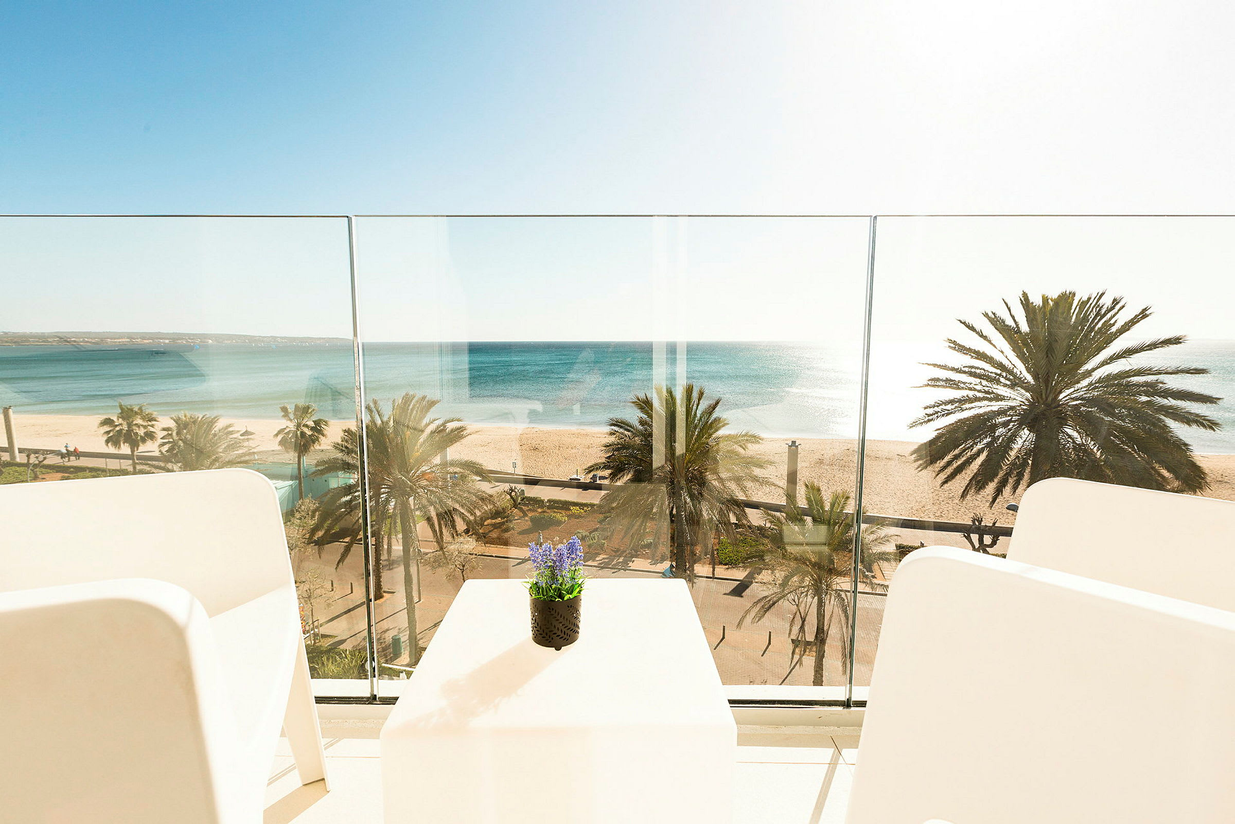 Udsigt fra en balkon mod havet og stranden med palmer. (AI-genereret tekst)