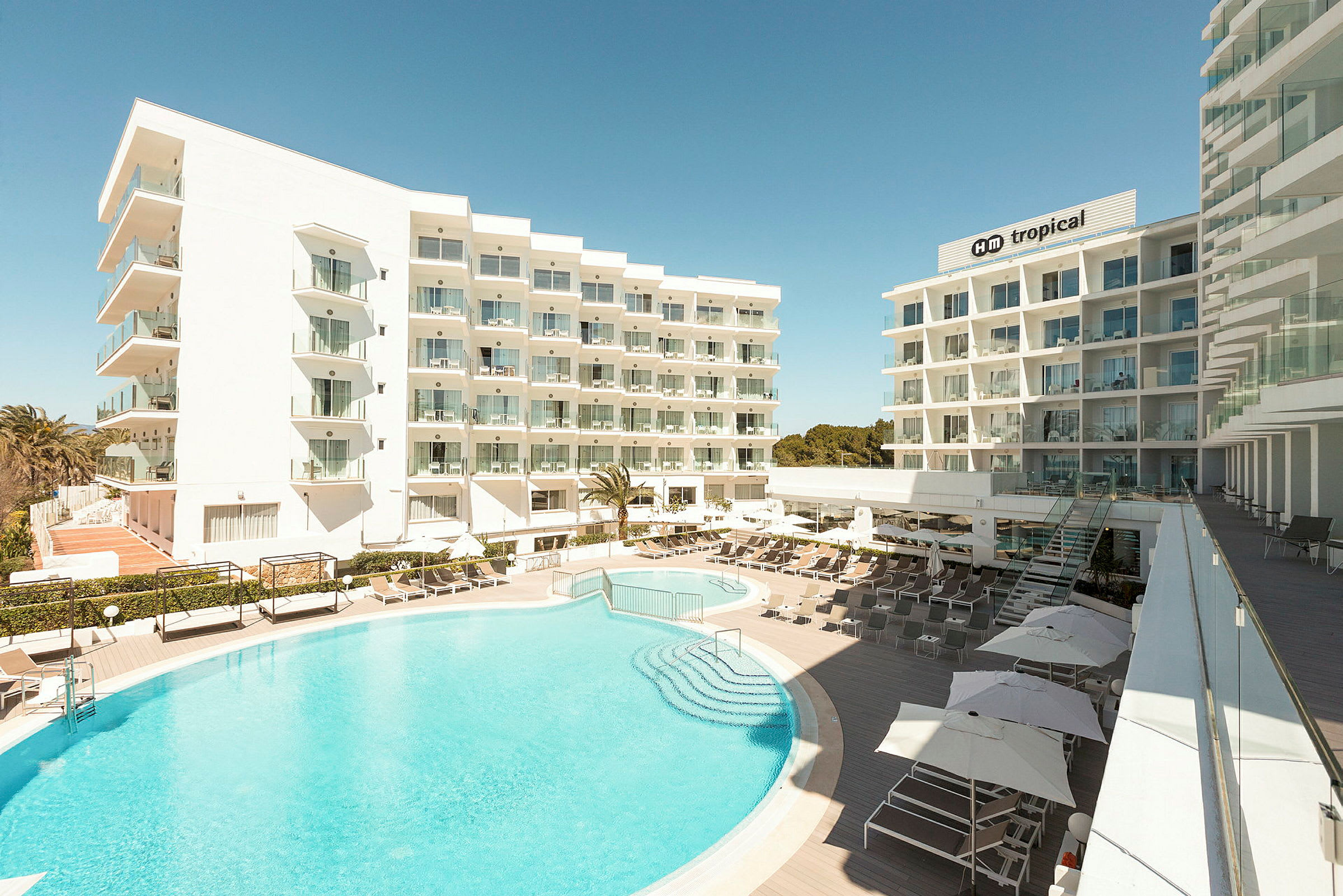 Billede af hotelbygninger med udendørs swimmingpool og liggestole. (AI-genereret tekst)
