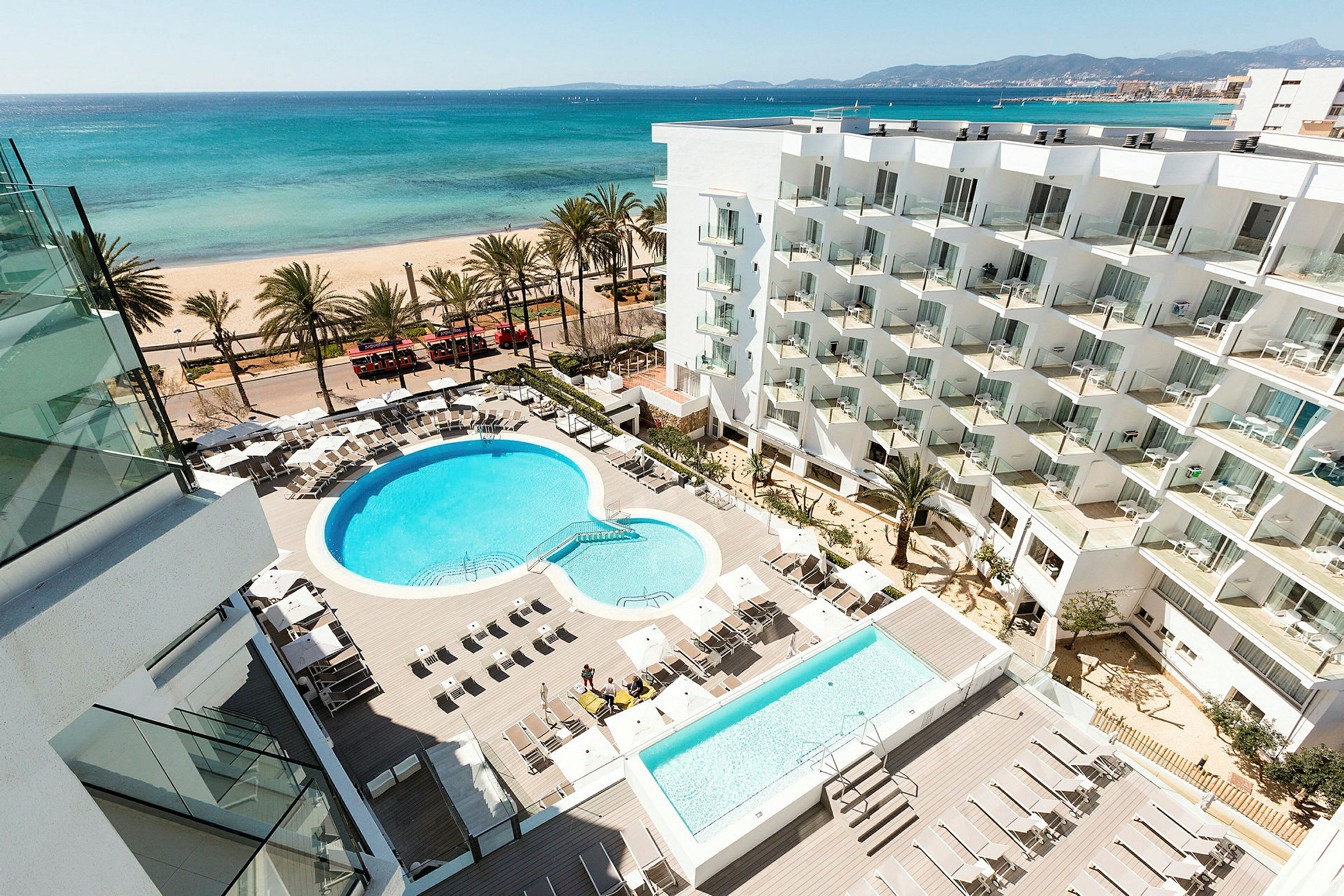 Hotelområde med pool og liggestole, strand og hav i baggrunden. (AI-genereret tekst)