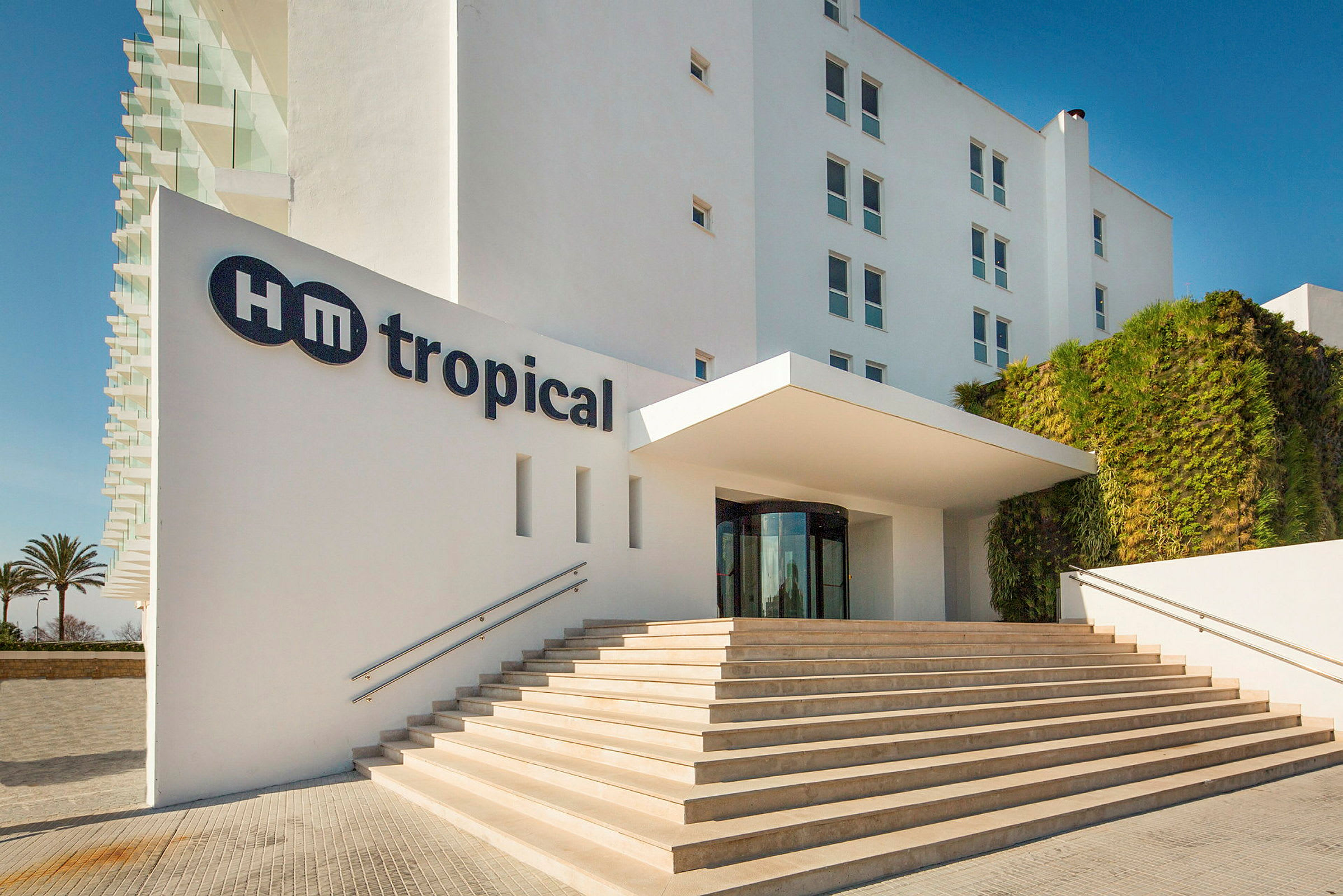 Billedet viser indgangen til HM Tropical hotel med trapper, der fører op til indgangen. (AI-genereret tekst)