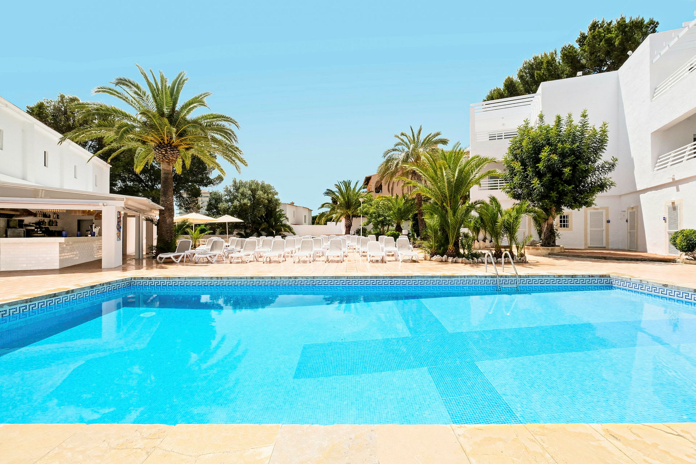 En udendørs swimmingpool omgivet af liggestole og palmer. (AI-genereret tekst)