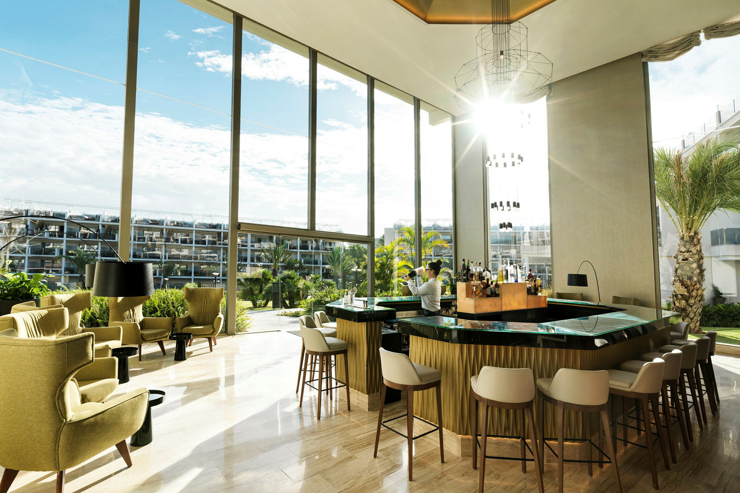 En elegant hotelbar med store vinduer og udsigt over en have. (AI-genereret tekst)