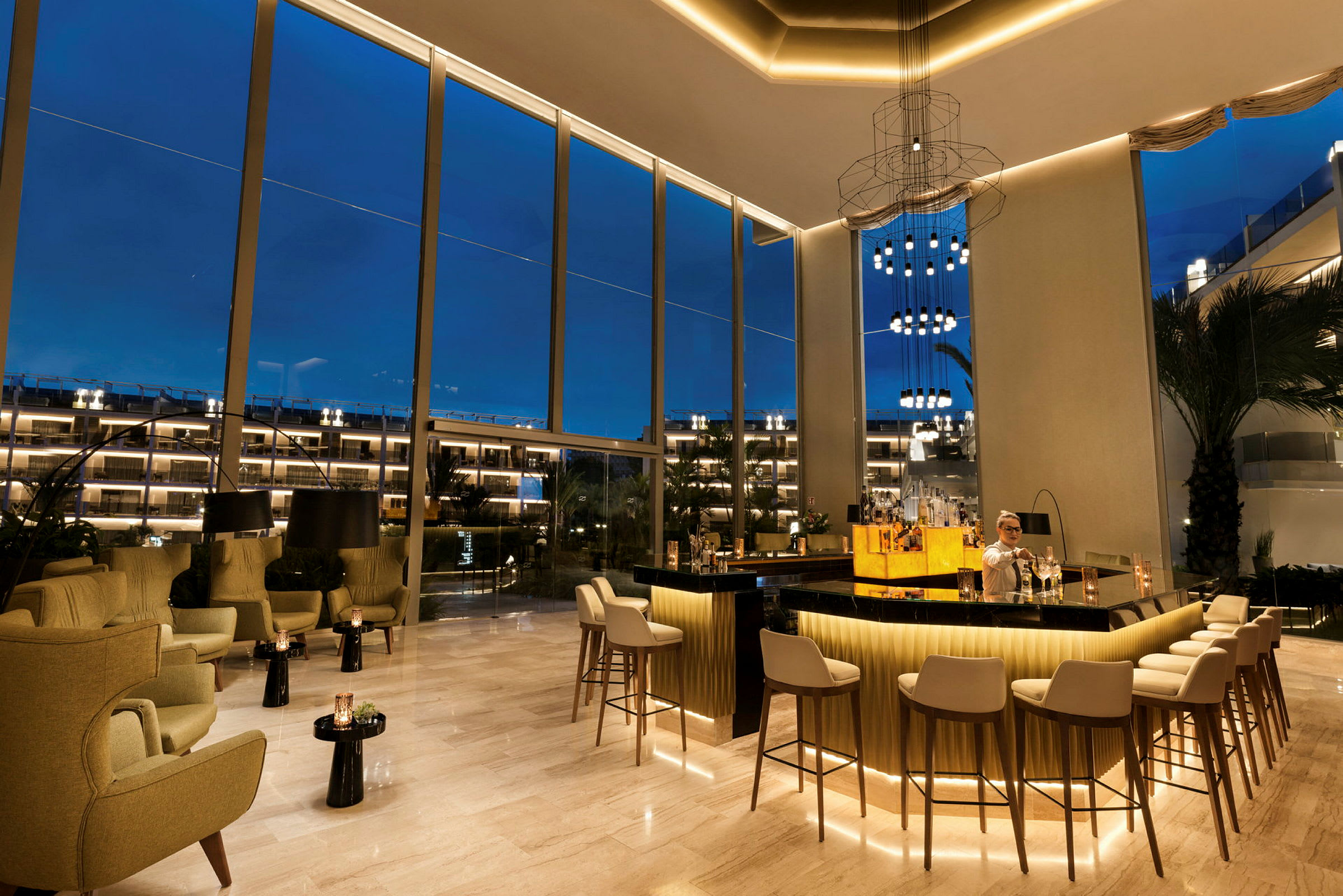 En elegant bar med siddepladser og høje vinduer, som vender mod udendørs belysning om aftenen. (AI-genereret tekst)