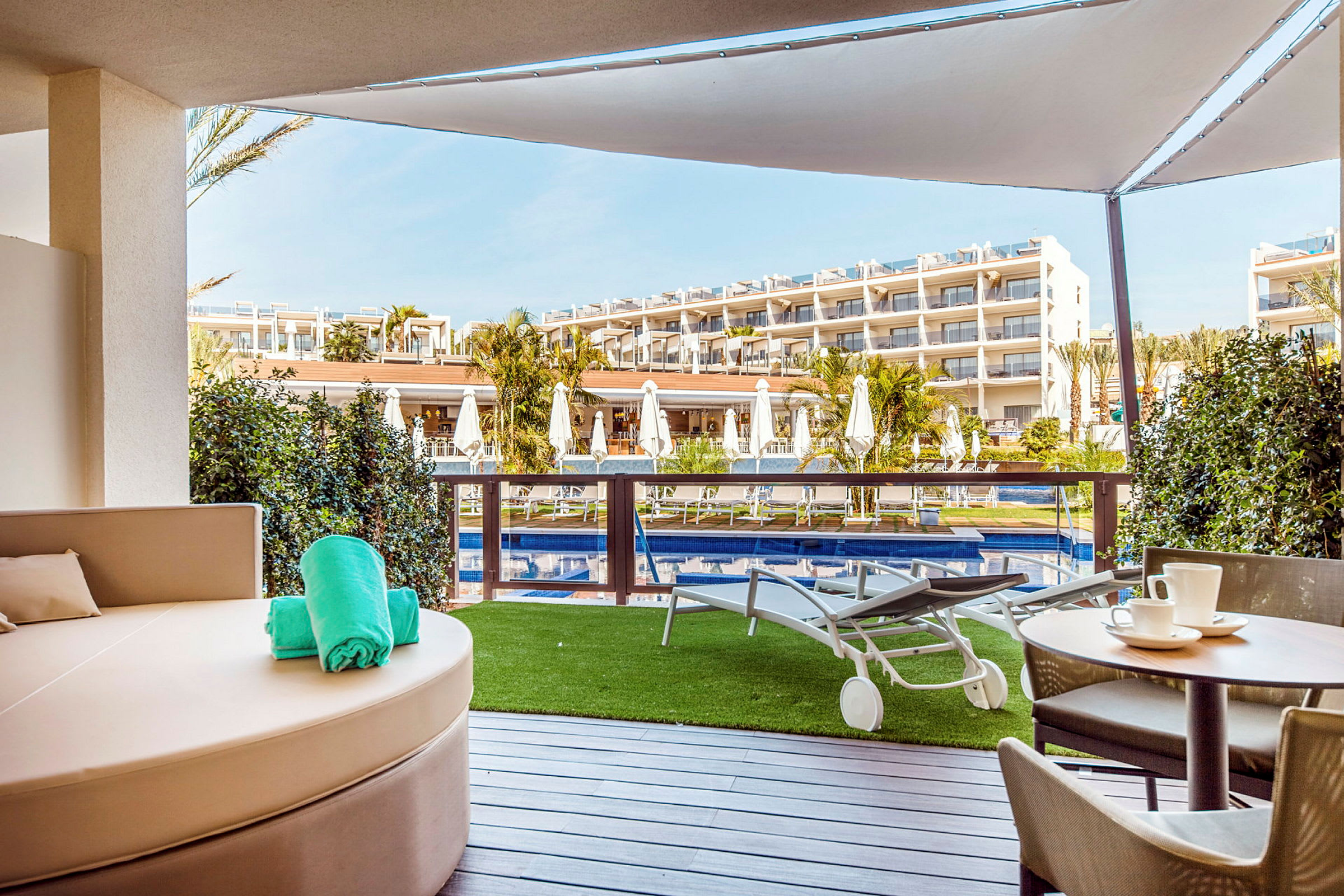 Udsigt fra terrasse med pool og liggestole foran hotelsbygning. (AI-genereret tekst)