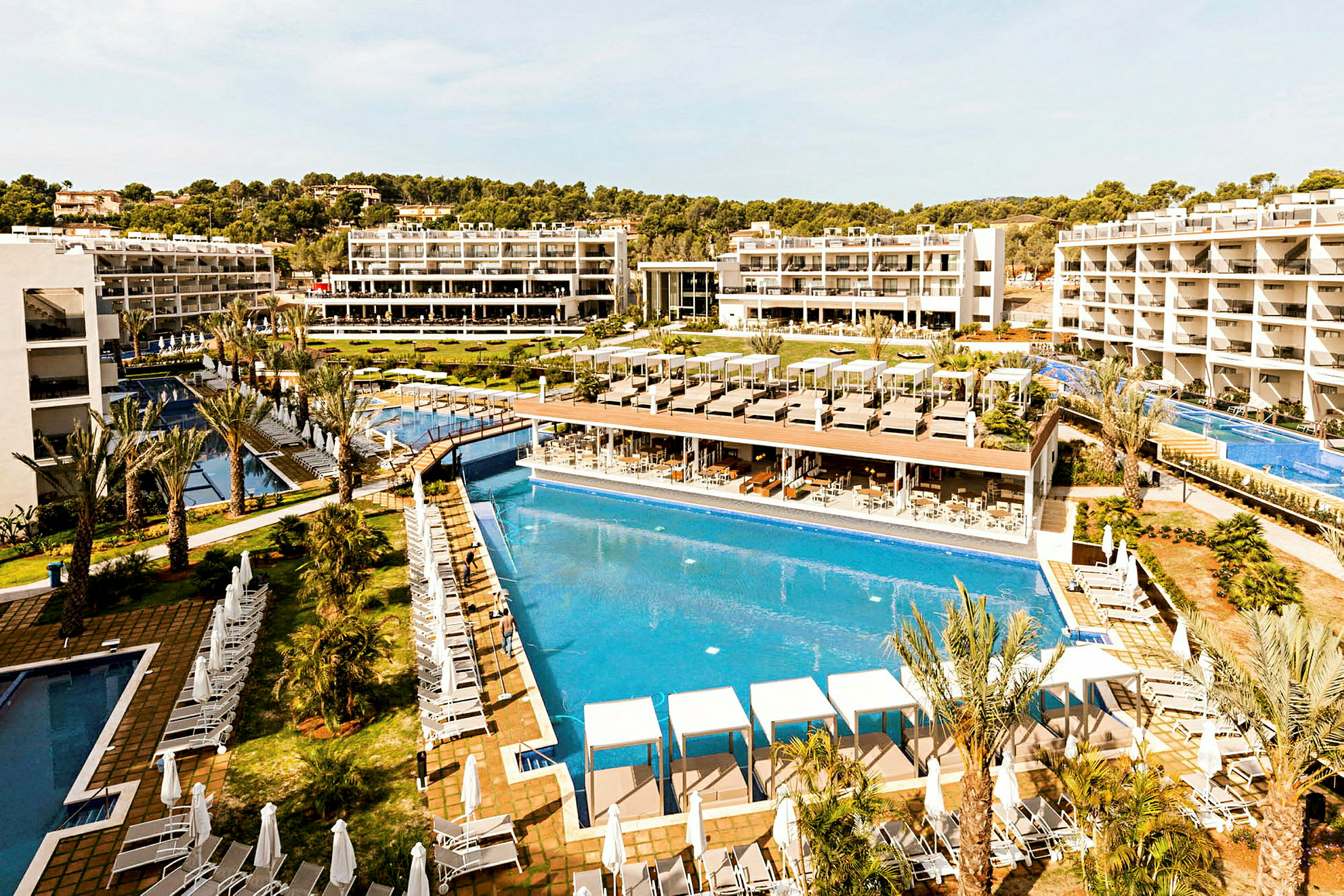 Et feriehotel med flere udendørs pools, liggestole og hvide bygninger i baggrunden. (AI-genereret tekst)
