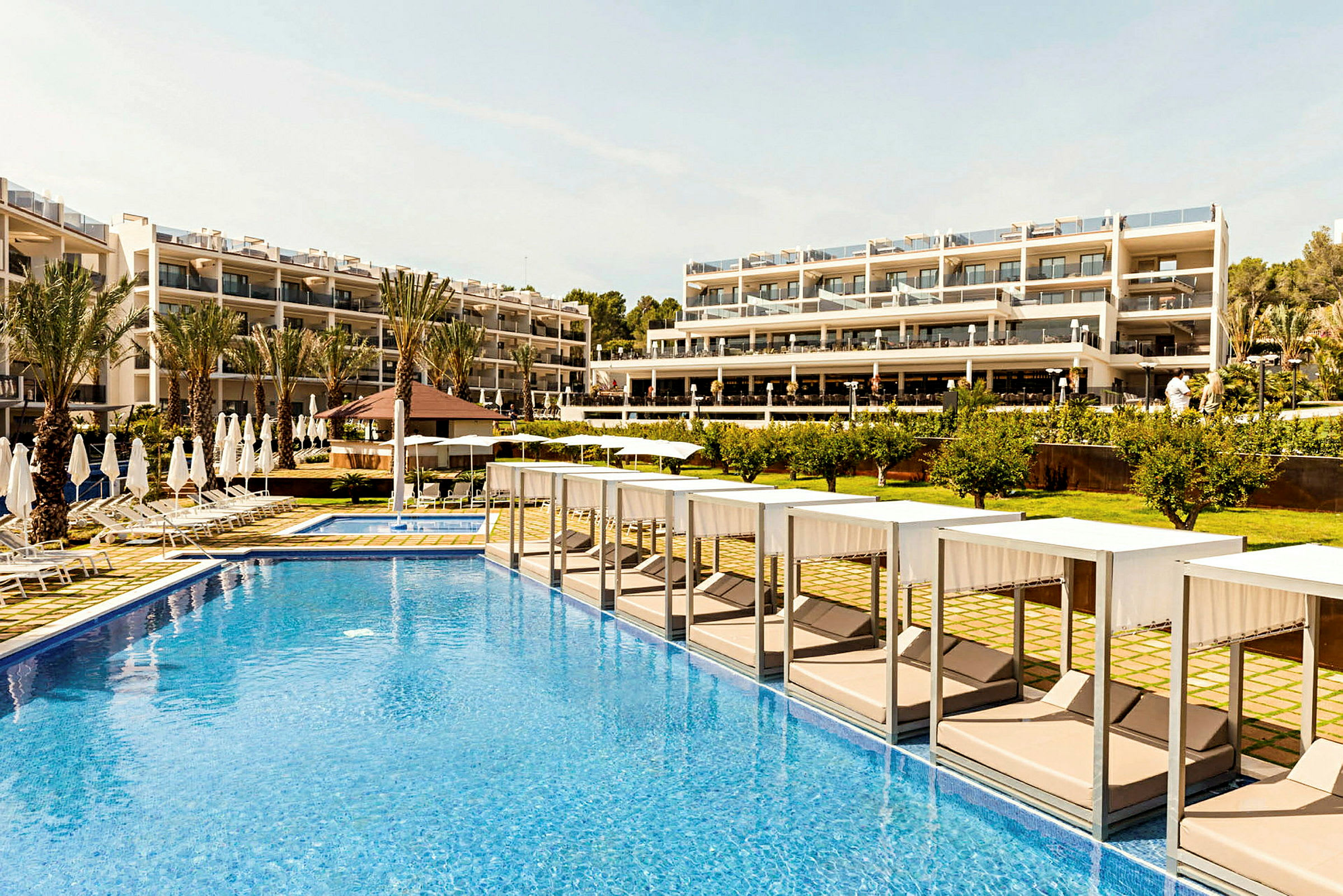 Hotelområde med pool, liggestole og bygning i baggrunden. (AI-genereret tekst)