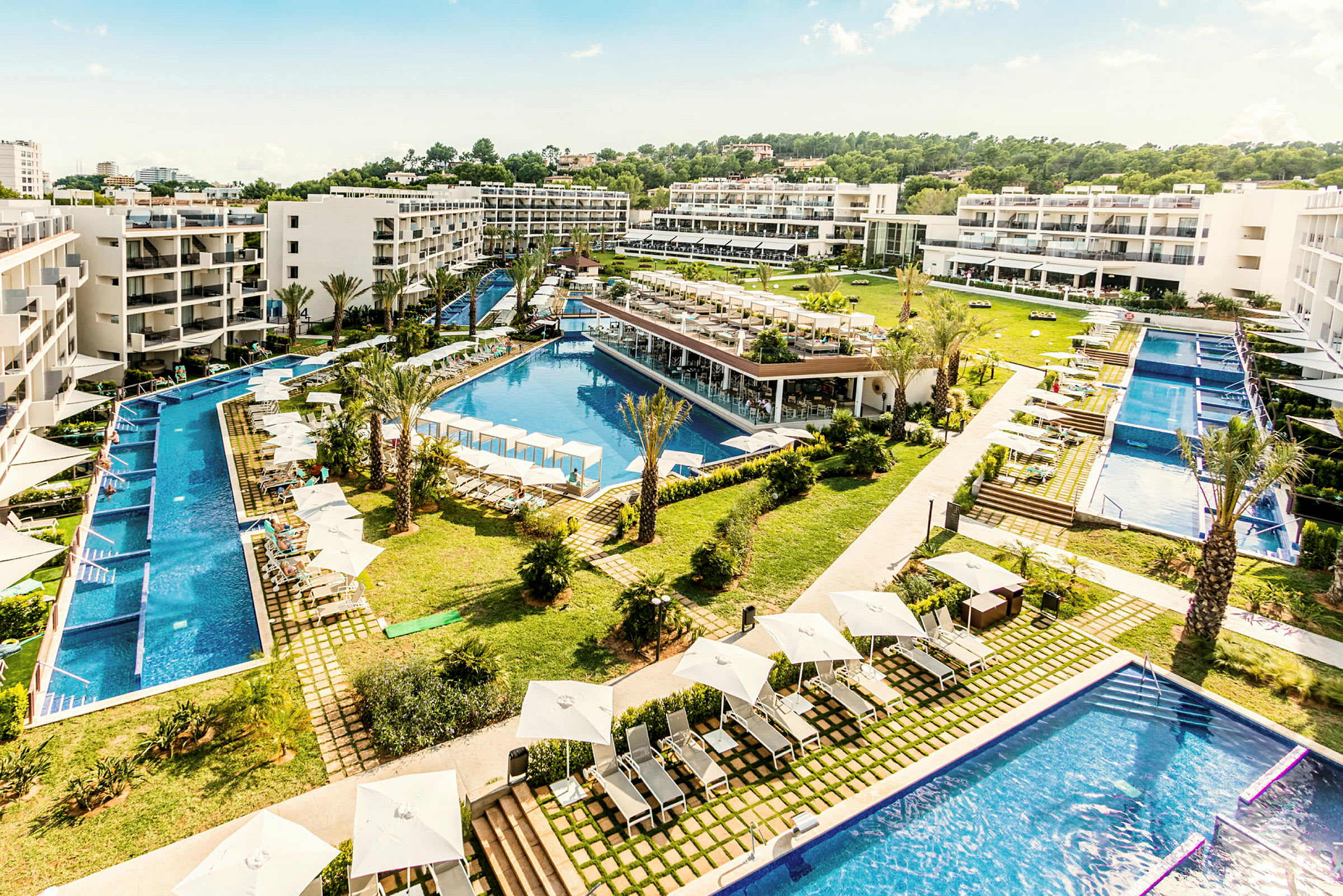 Hotelkompleks med pools, liggestole og grønt område. (AI-genereret tekst)