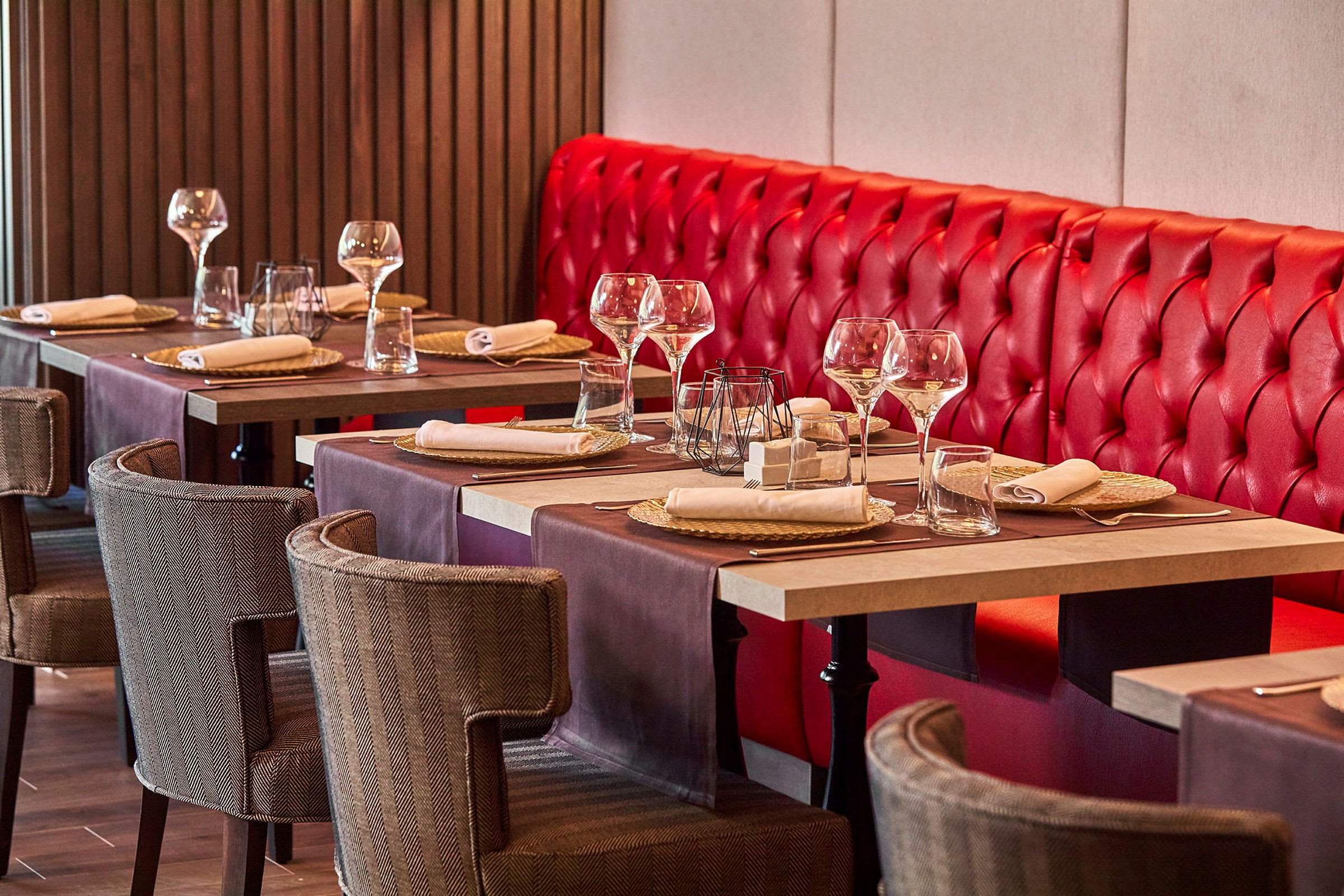 Et restaurantbord med rødt bænksæde og opdækkede borde med glas og servietter. (AI-genereret tekst)