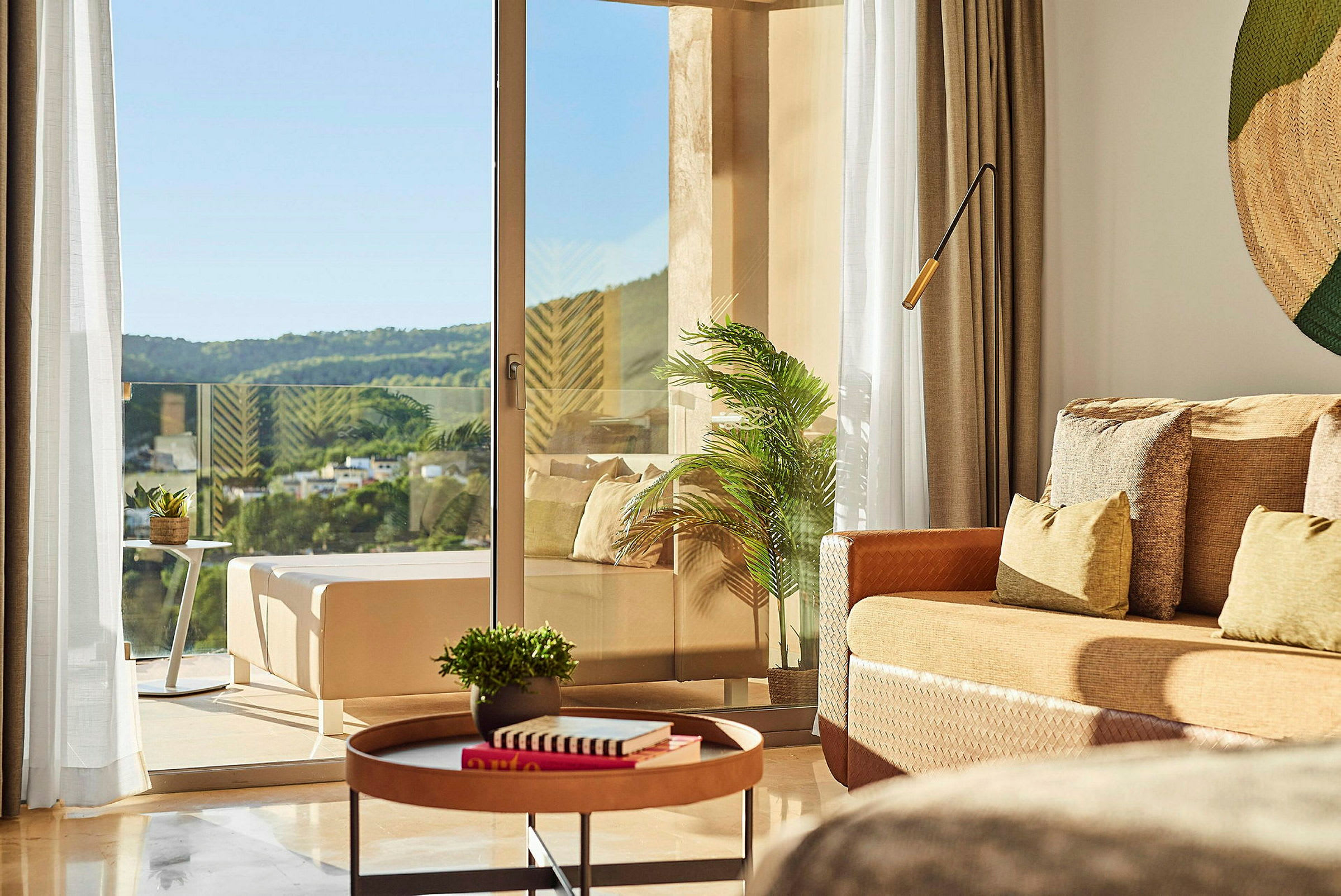 Et lyst og moderne hotelværelse med bord, planter og udsigt til naturen fra balkonen. (AI-genereret tekst)