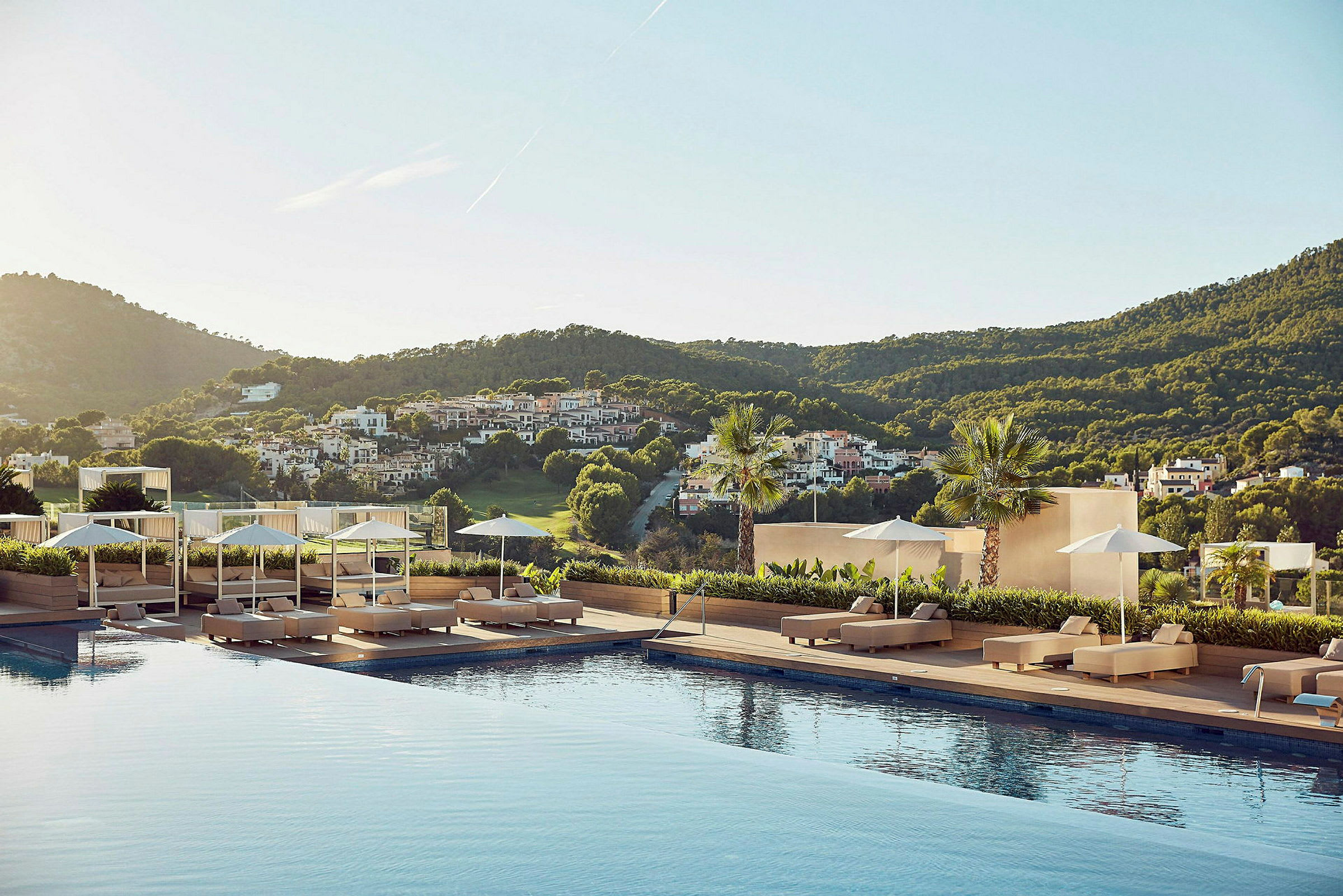 En udsigt fra et hotelområde med en pool omgivet af liggestole, parasoller og et frodigt landskab i baggrunden. (AI-genereret tekst)