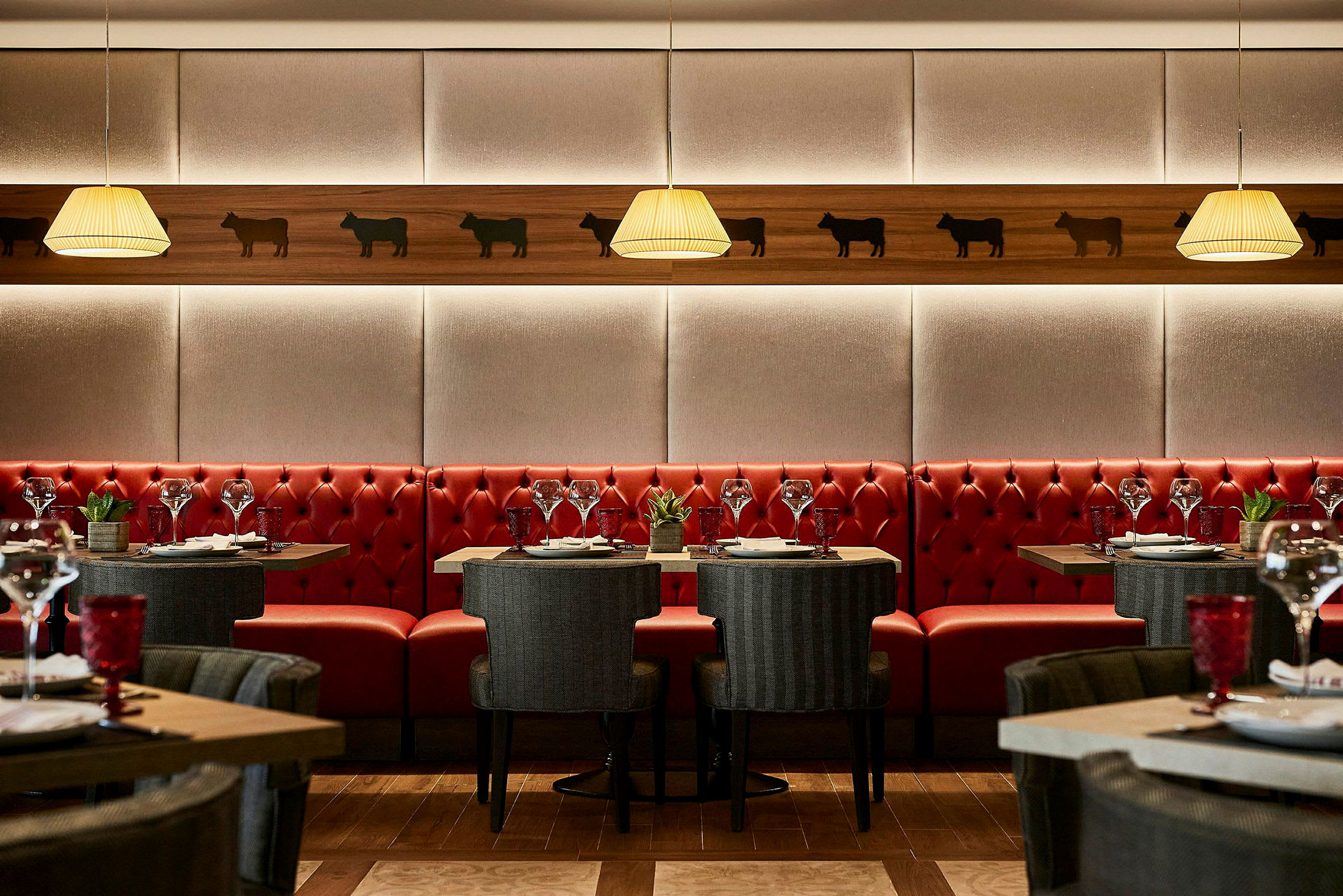 Restaurantinteriør med røde sofaer, elegante borde og stole samt vægdekorationer. (AI-genereret tekst)