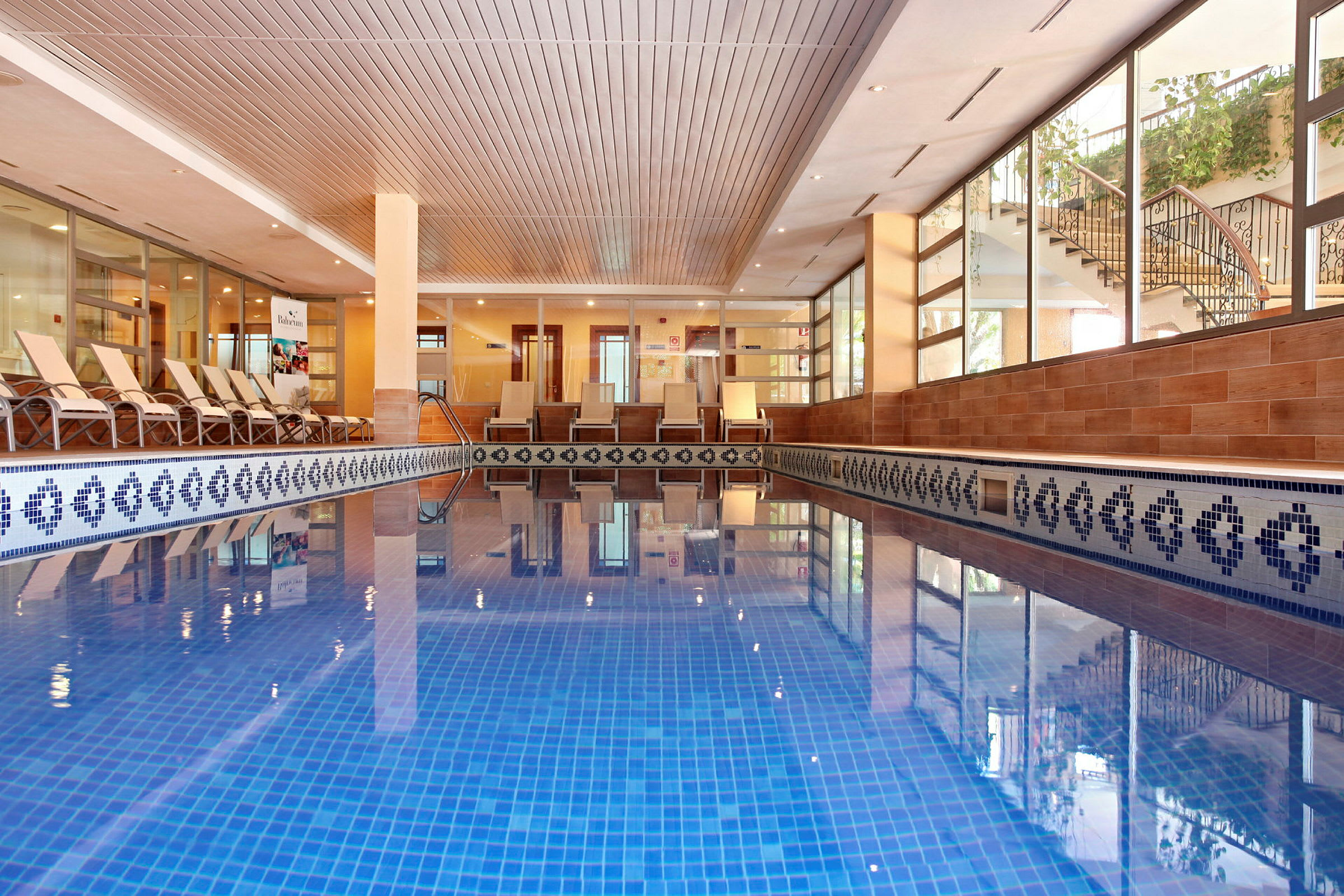 Indendørs pool med blå fliser og liggestole langs siden. (AI-genereret tekst)