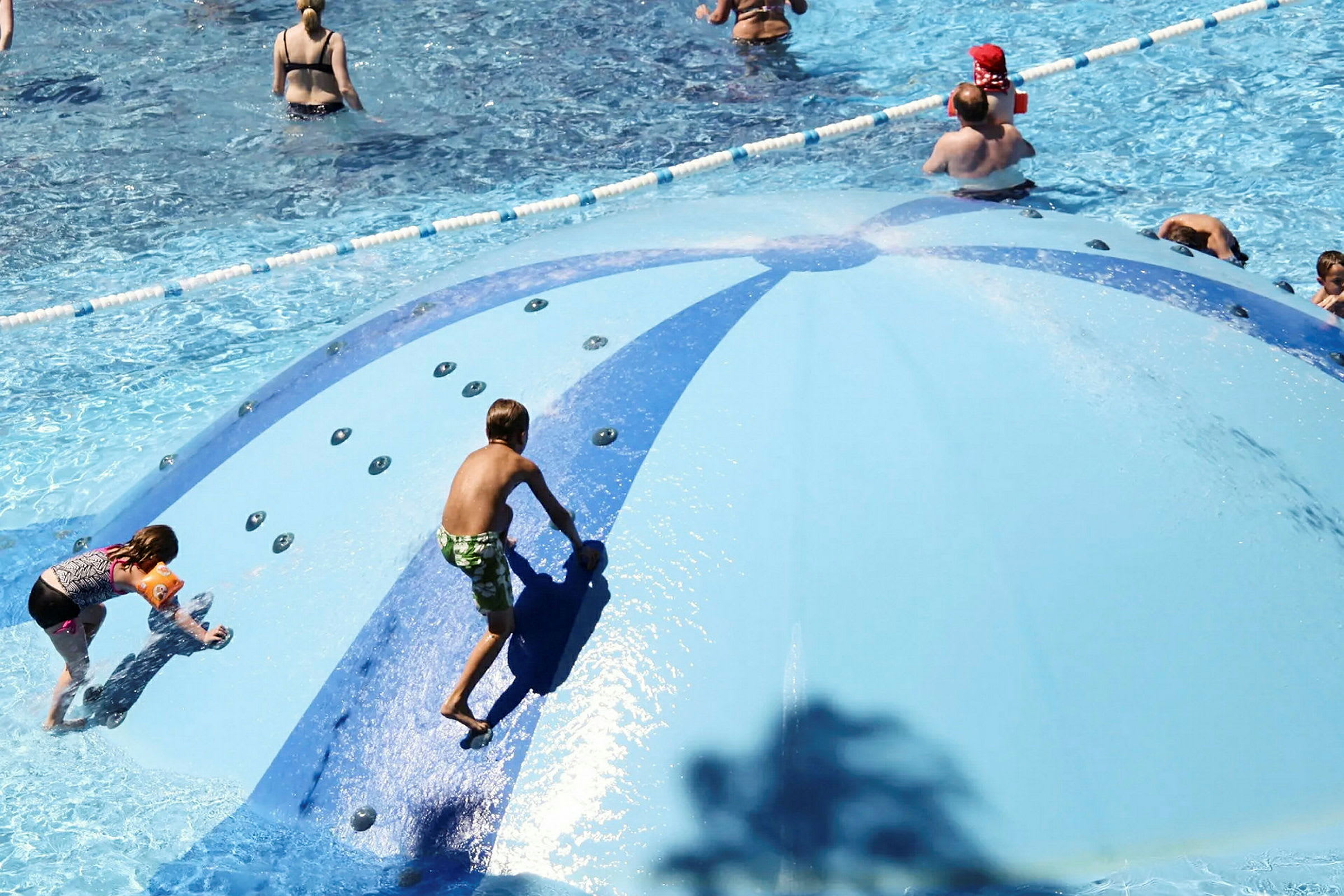 Børn leger på en blå vandrutschebane i en pool. (AI-genereret tekst)