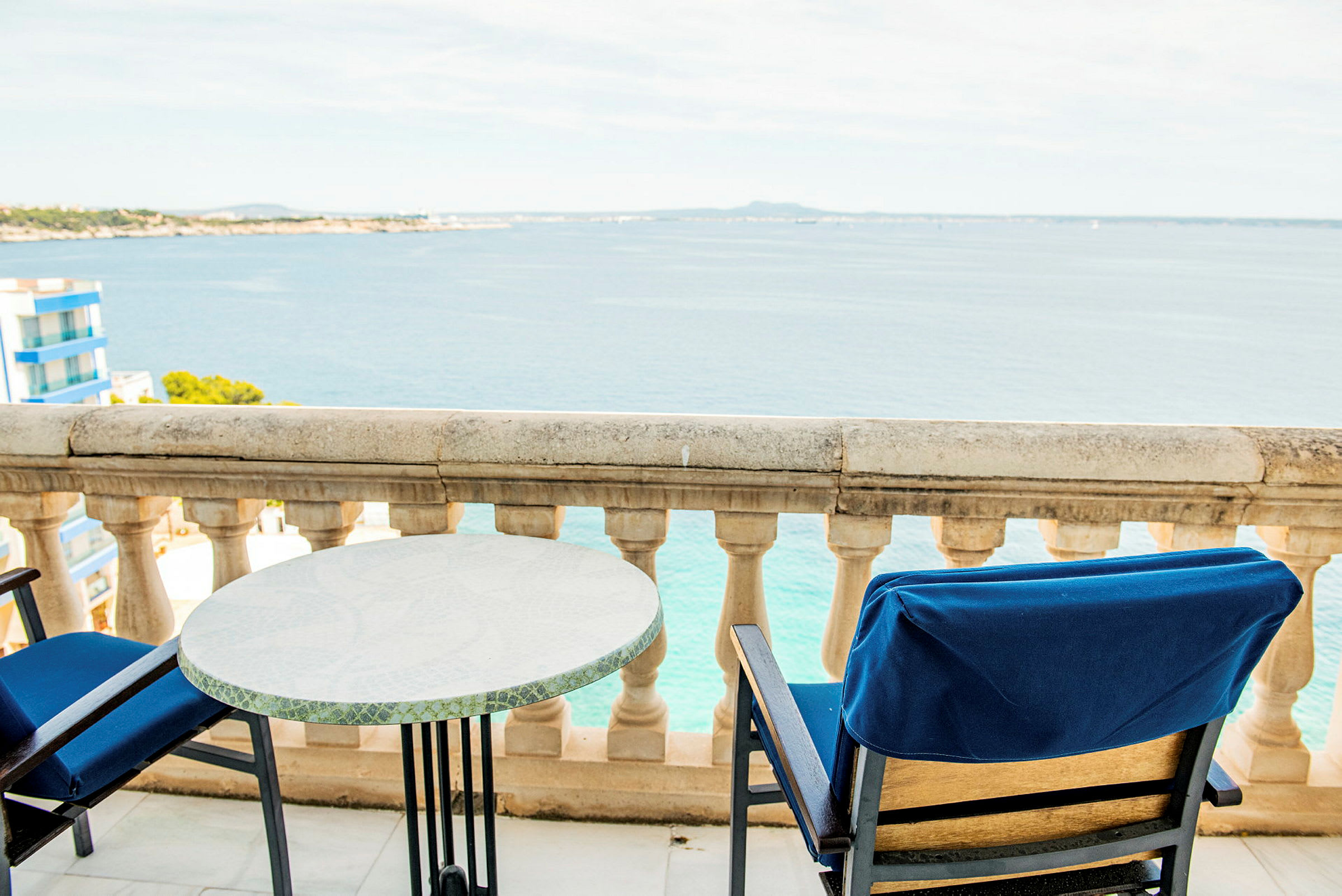 Udsigt fra en altan med havudsigt, bord og stole. (AI-genereret tekst)
