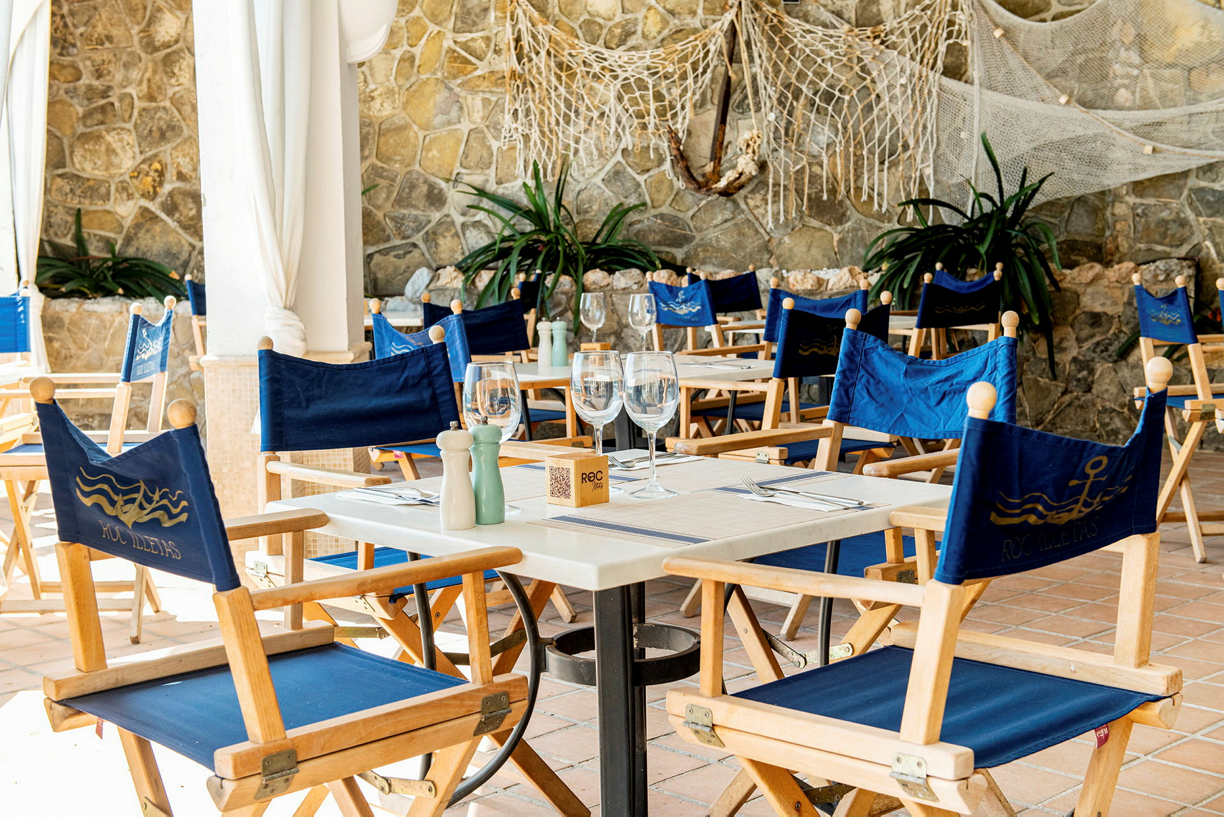 Et bord med blå stole på en restaurant med stenvæg i baggrunden. (AI-genereret tekst)