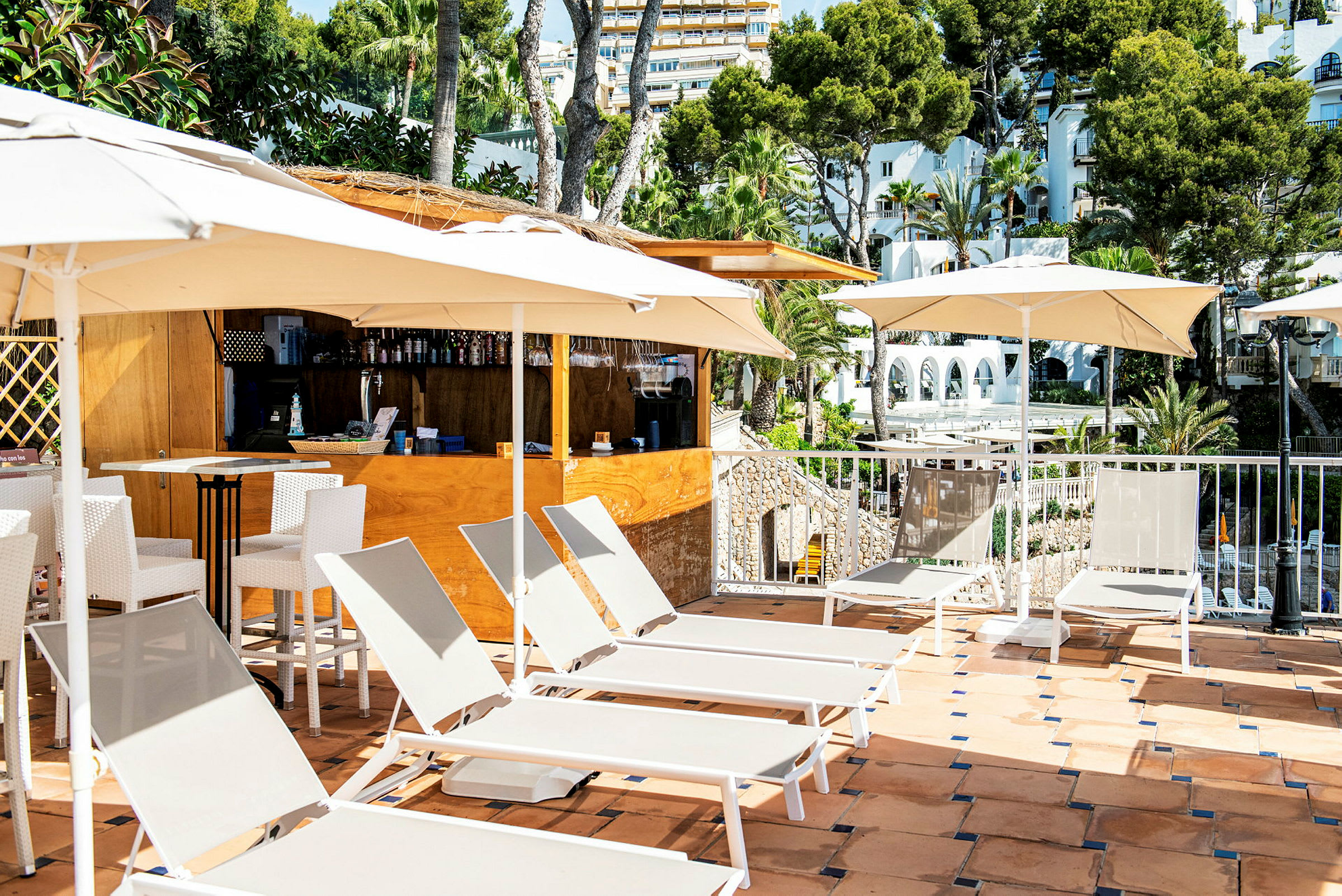 Liggestole og parasoller på en terrasse ved en bar med udsigt over træer og bygninger. (AI-genereret tekst)