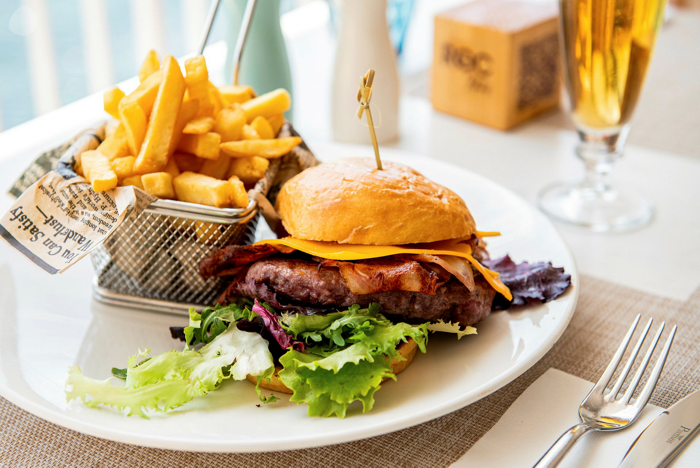 En tallerken med en hamburger med ost, bacon og salat samt en kurv med pommes frites. (AI-genereret tekst)