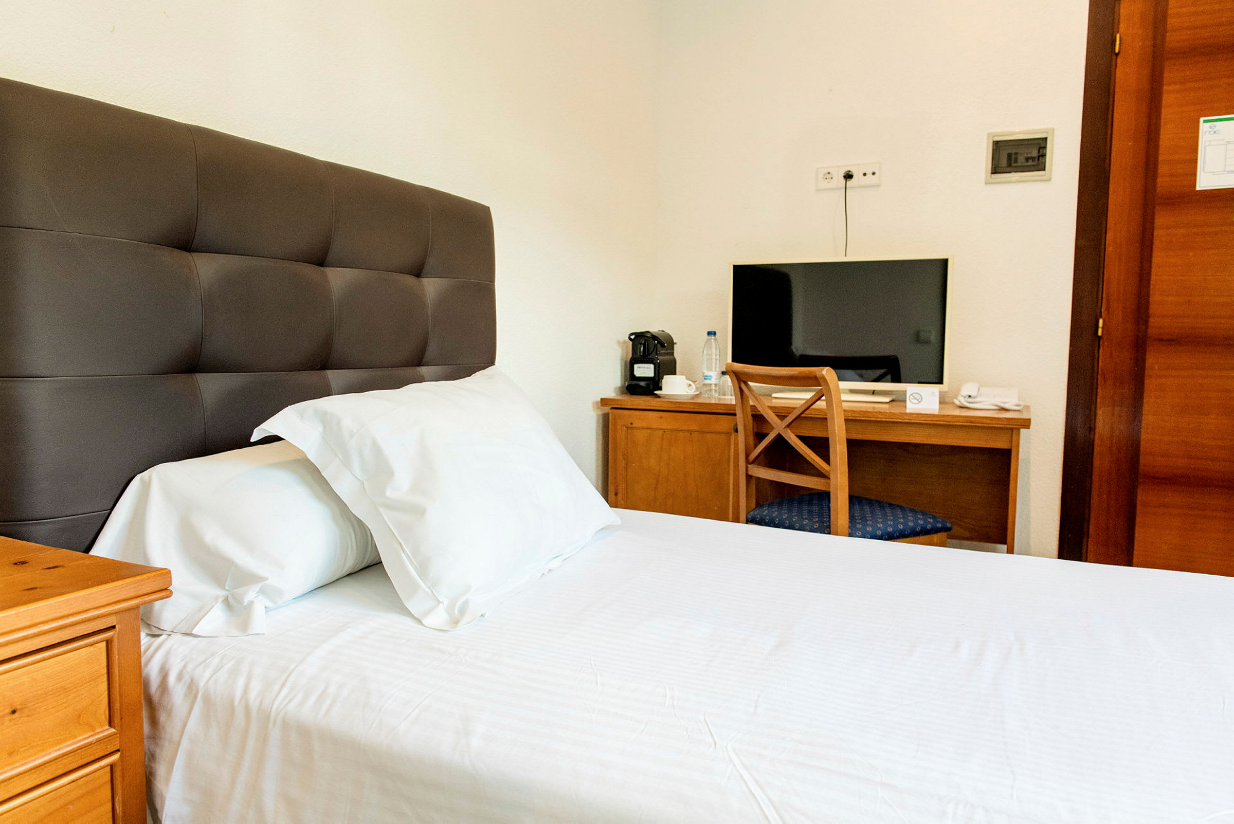 Hotelværelse med en seng og et skrivebord med en stol og et tv. (AI-genereret tekst)