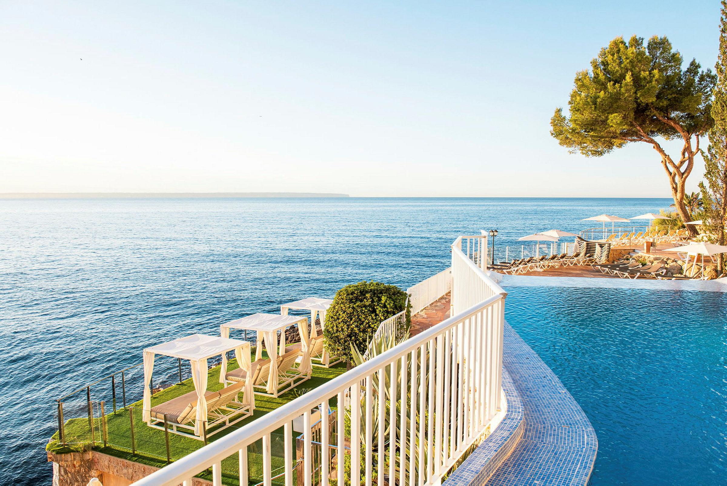 En infinitypool ved havet med liggestole og omgivende grønne områder. (AI-genereret tekst)