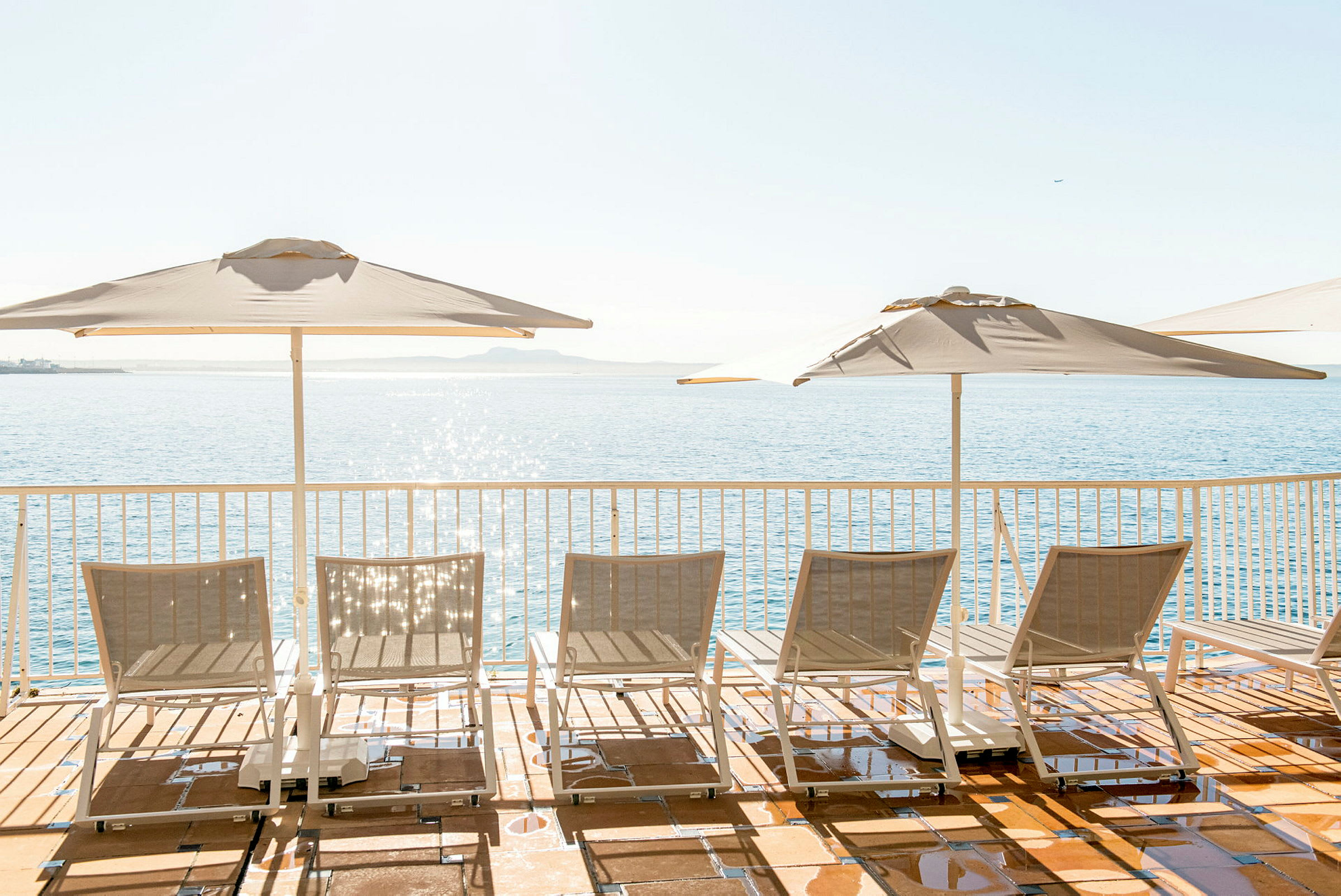 Solsenge og parasoller på en terrasse med udsigt over havet. (AI-genereret tekst)
