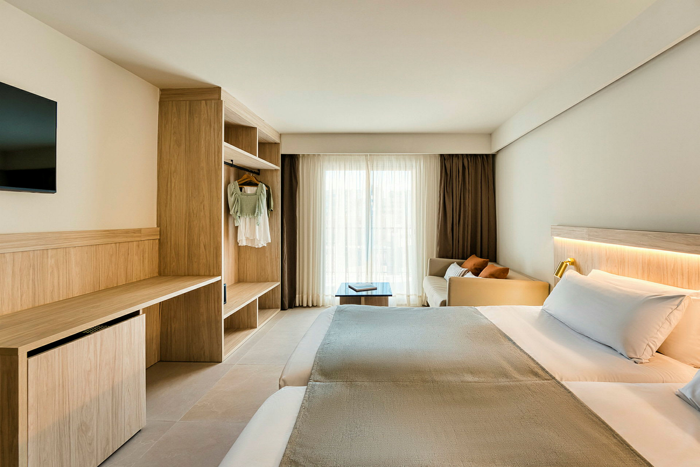 Et hotelværelse med en dobbeltseng, skrivebord og garderobe. Vindue dækket med lyse gardiner. (AI-genereret tekst)