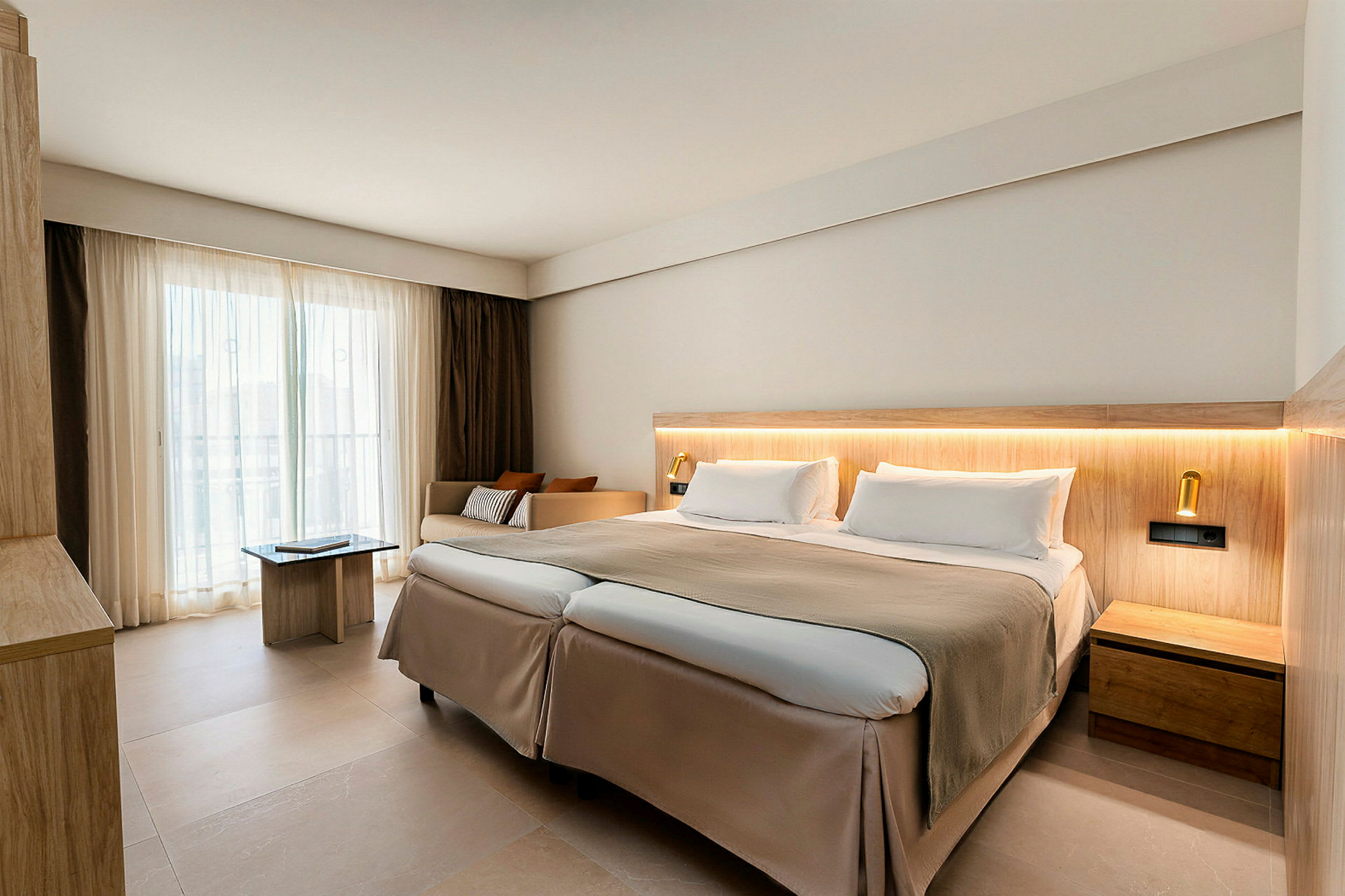 Et moderne hotelværelse med en dobbeltseng, lyse farver og store vinduer med gardiner. (AI-genereret tekst)