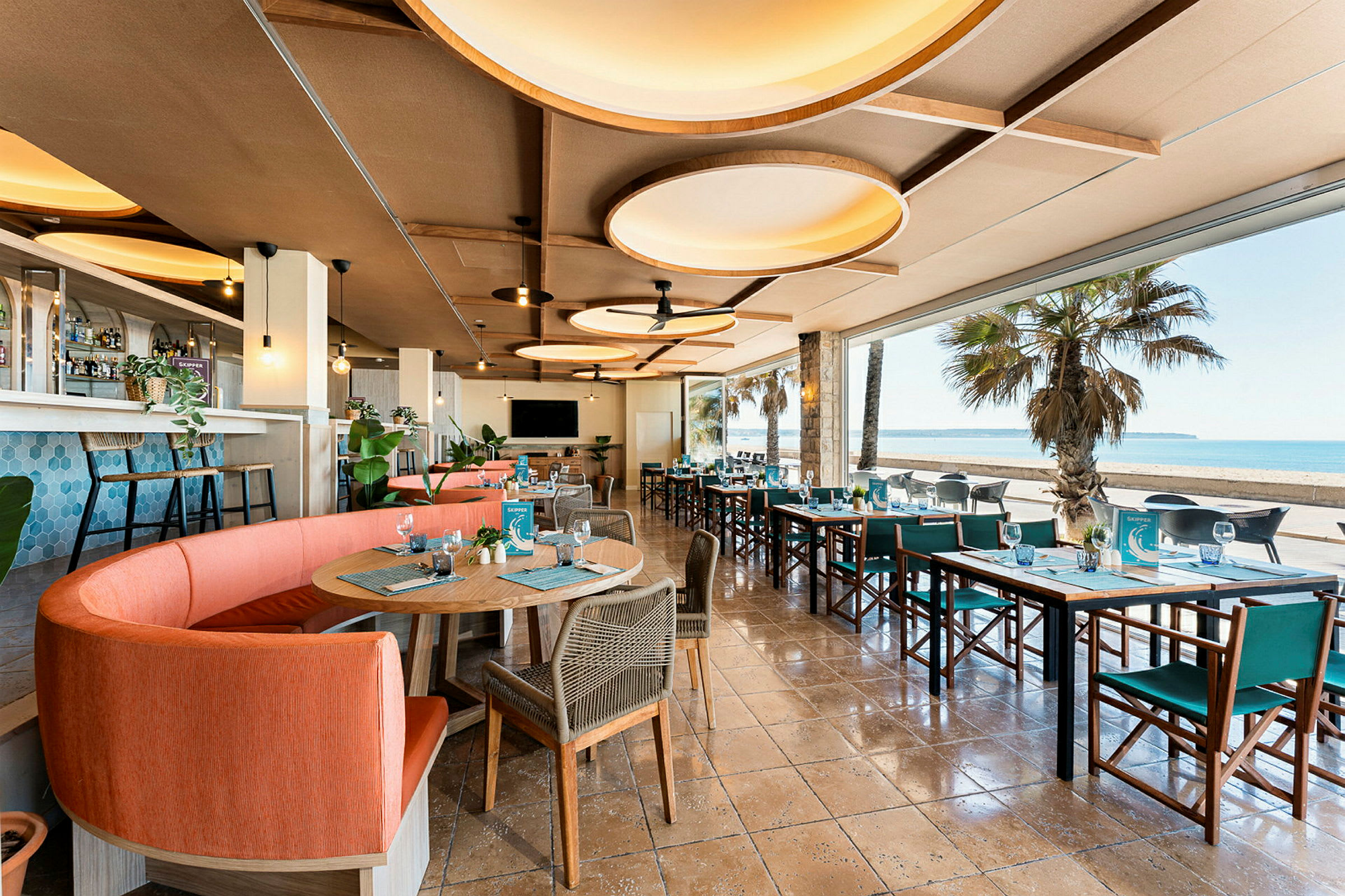 Restaurant med moderne møbler og store vinduer ud mod en strand. (AI-genereret tekst)