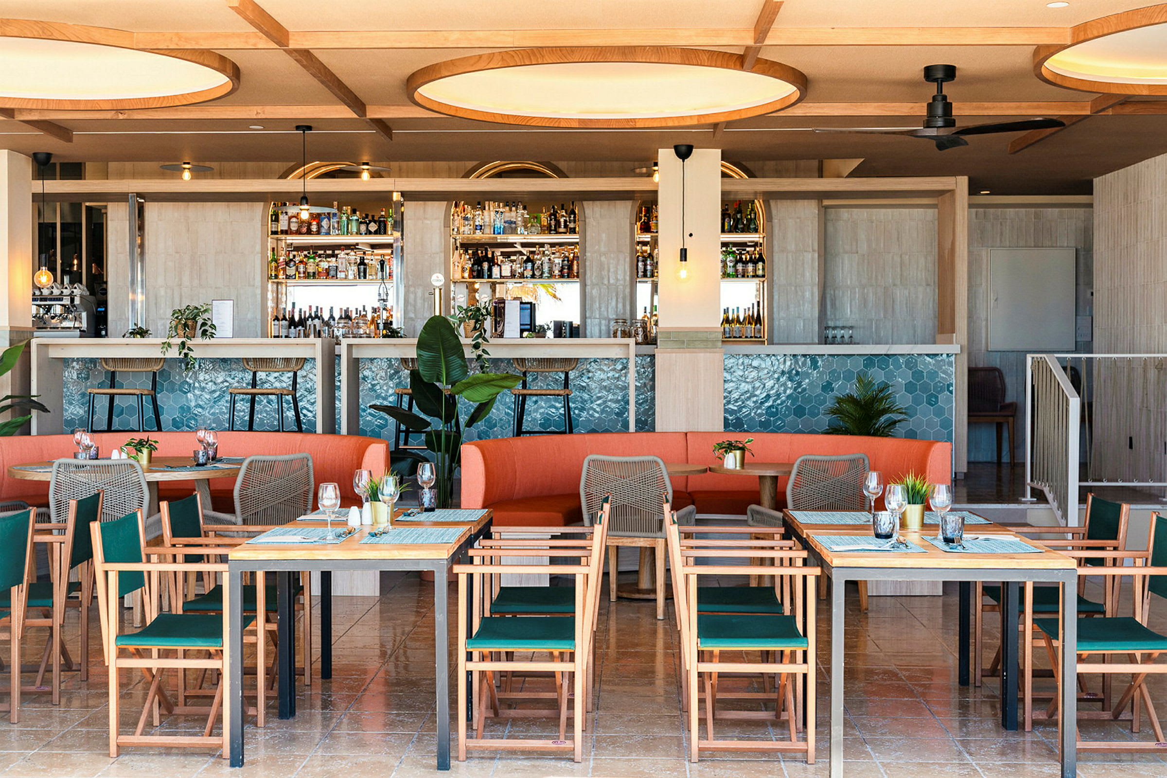 Billede af en moderne restaurant med borde, stole og en orange sofa samt en bardisk dekoreret med blå fliser. (AI-genereret tekst)