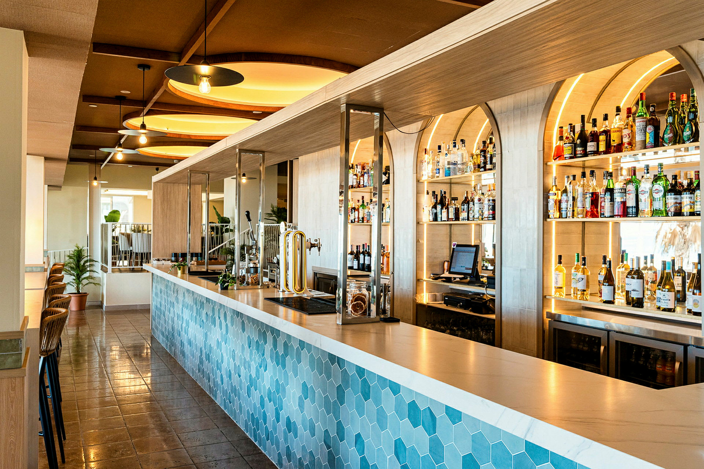 En moderne bar med en blå sekskantet mønstret bardisk og hylder fyldt med flasker og drikkevarer i baggrunden. (AI-genereret tekst)