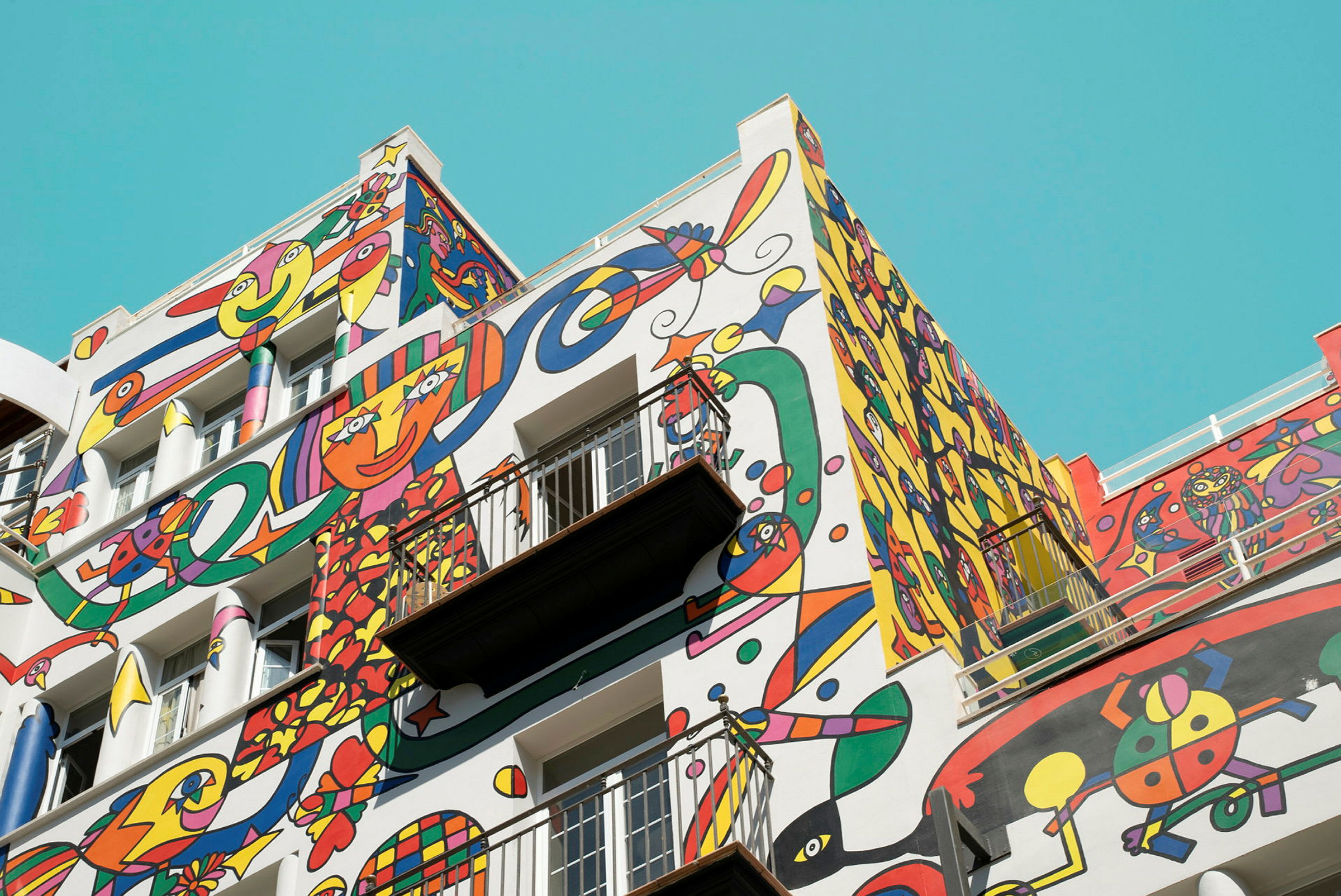 En bygningsfacade dækket med farverige, abstrakte kunstmotiver mod en klar blå himmel. (AI-genereret tekst)