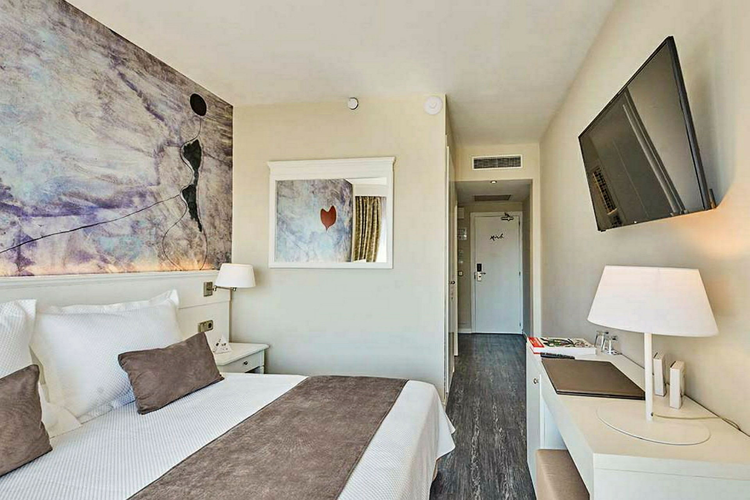 Et moderne hotelværelse med en dobbeltseng, vægkunst, skrivebord og fladskærms-tv. (AI-genereret tekst)