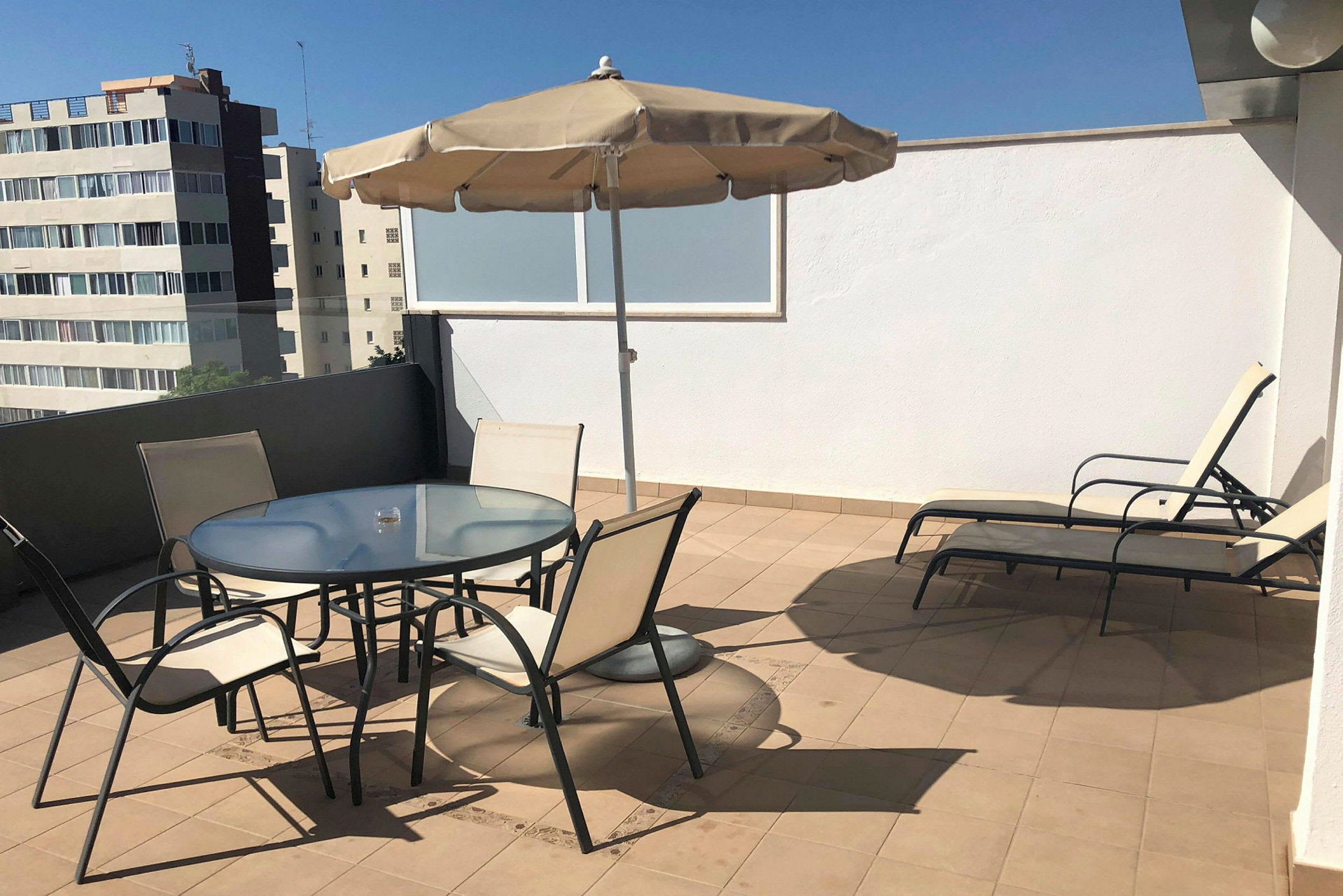 En tagterrasse med et bord og fire stole under en parasol samt to liggestole ved siden af. (AI-genereret tekst)
