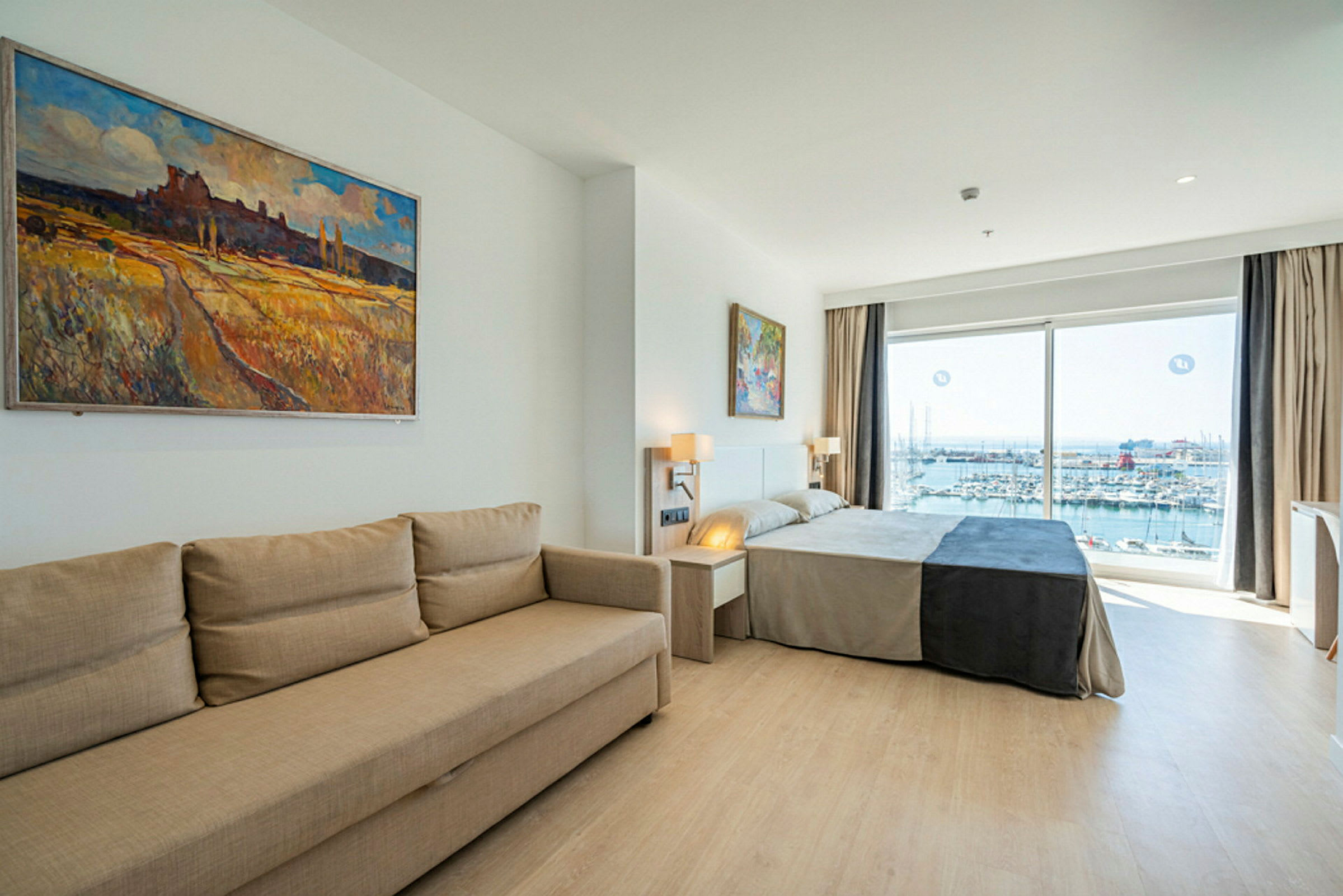 Et hotelværelse med en sofa, en seng og vinduer, der viser udsigt over en marina. (AI-genereret tekst)