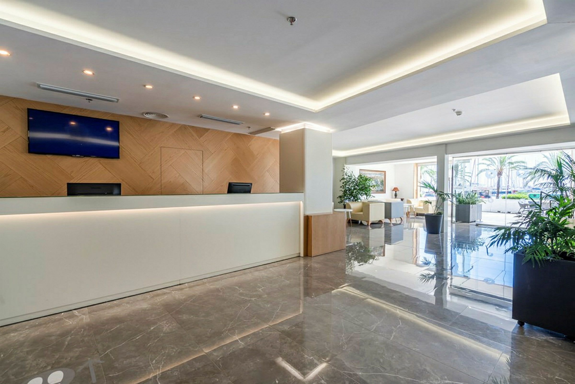 Receptionen i et moderne hotel med marmorgulv og hvide vægge, og der er et komfortabelt siddeområde ved siden af. (AI-genereret tekst)