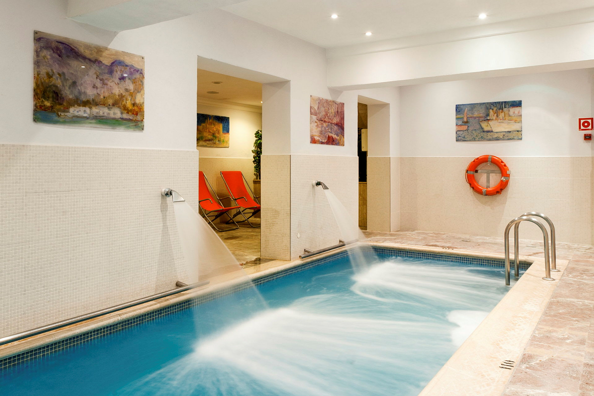 Indendørs pool med vandstråler og orange liggestole i baggrunden. (AI-genereret tekst)