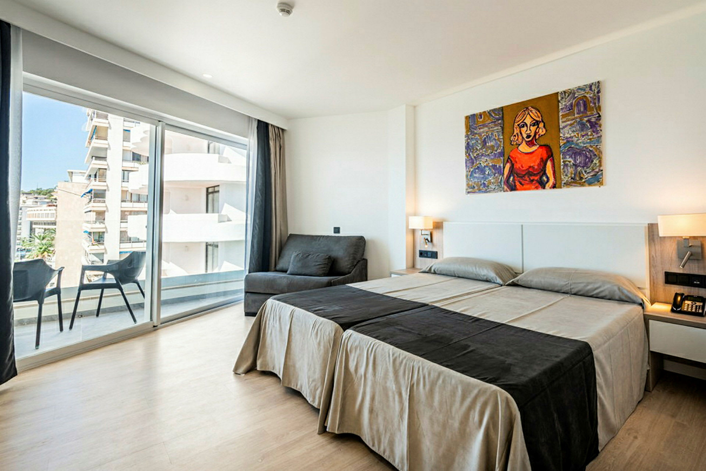 Et hotelværelse med to enkeltsenge, en sofa, en balkon og store glasvinduer. (AI-genereret tekst)