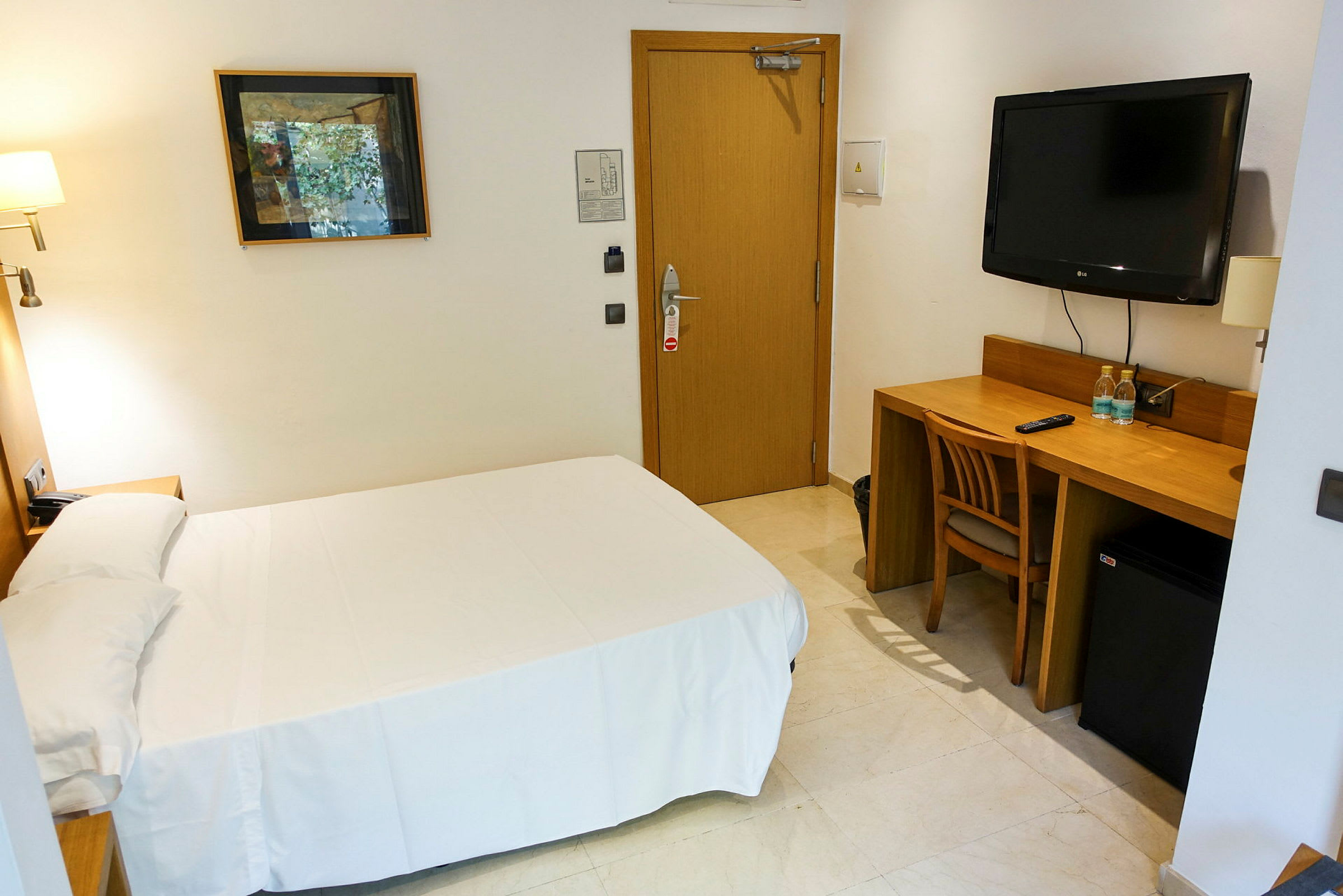 Et enkelt hotelværelse med en seng, skrivebord og stol. På væggen er der et fjernsyn og et kunstværk. (AI-genereret tekst)