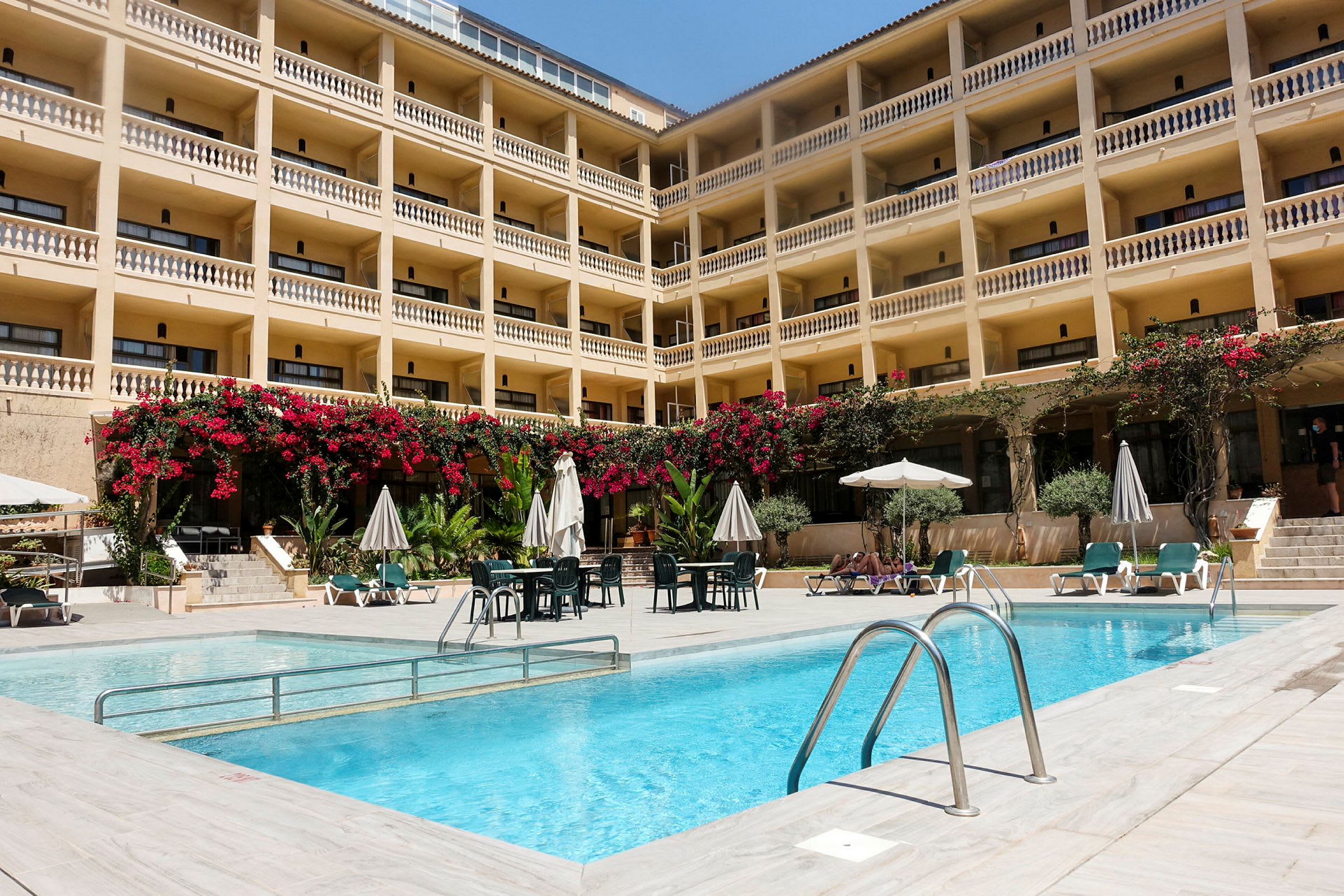 Billede af et hotel med en udendørs pool og liggestole foran. (AI-genereret tekst)