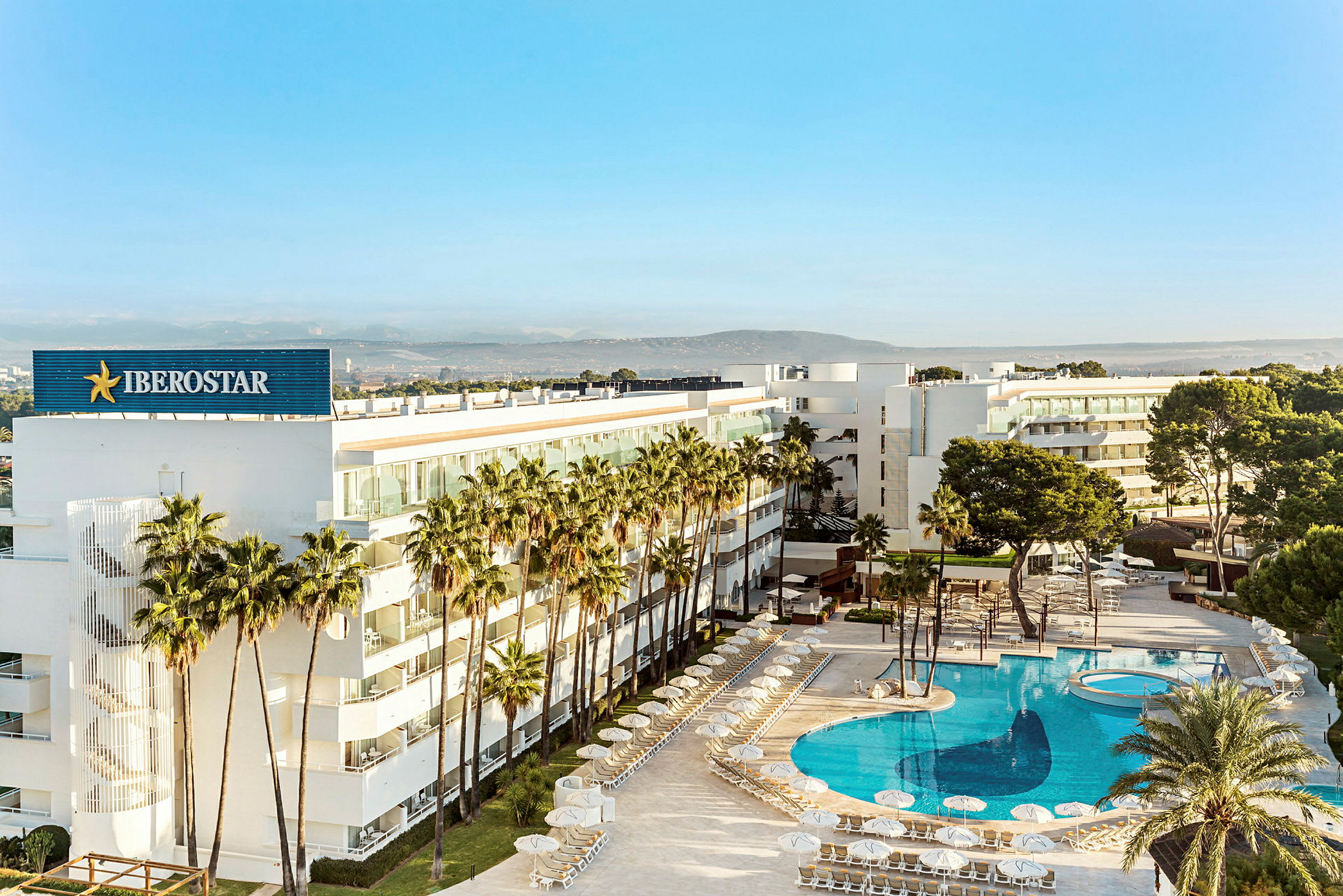 Et moderne hotel omgivet af palmer med en stor, klarblå pool. (AI-genereret tekst)