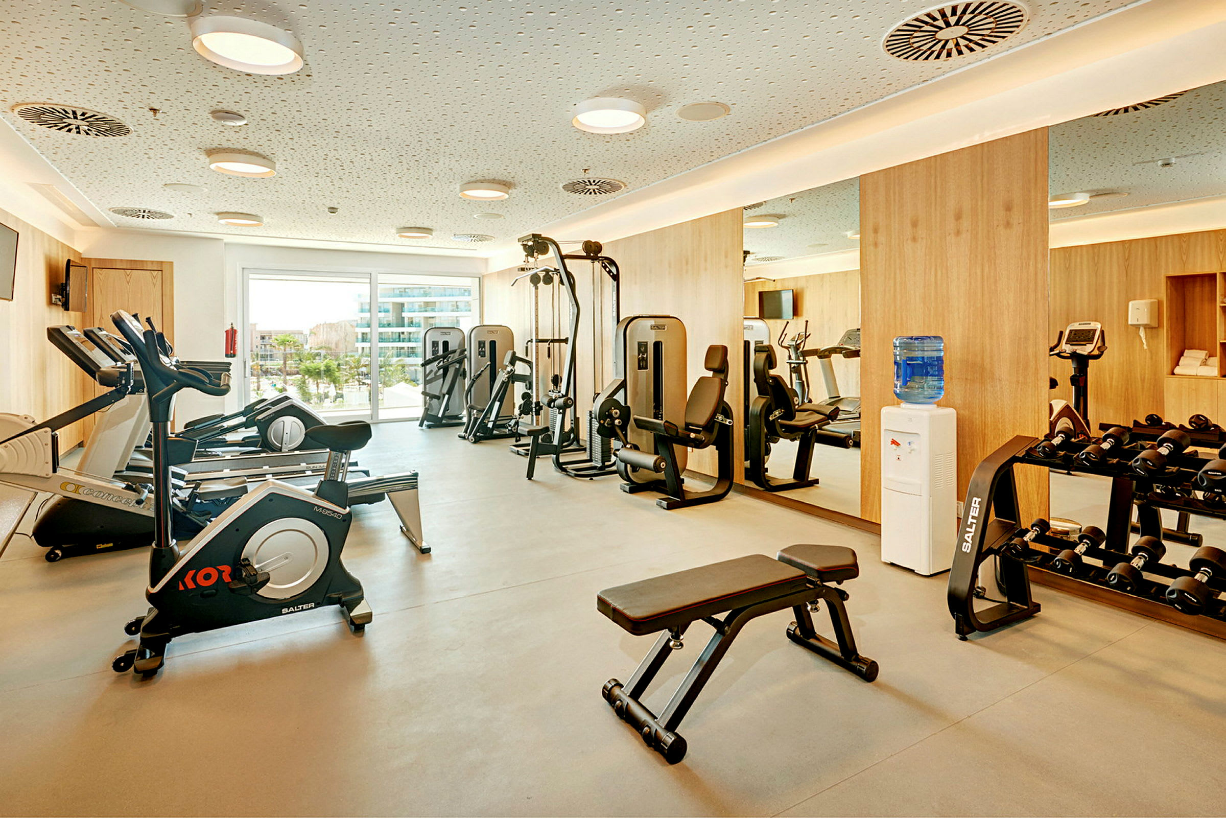Et fitnesscenter med træningsudstyr, herunder løbebånd, styrketræningsmaskiner og håndvægte. (AI-genereret tekst)