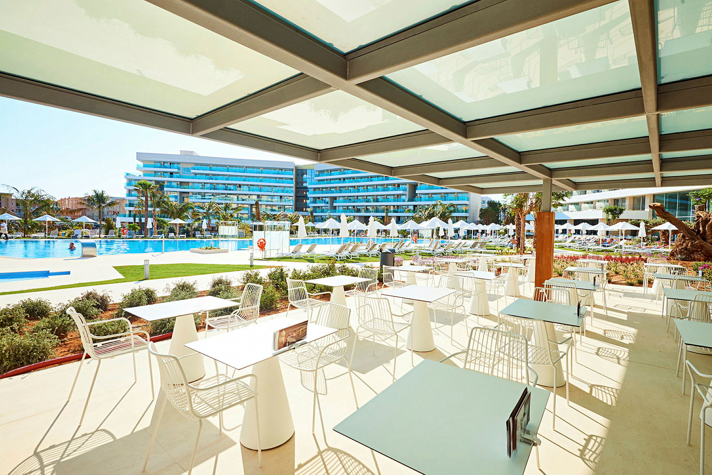 Udendørs siddepladser med udsigt til en pool og hotelbygninger. (AI-genereret tekst)